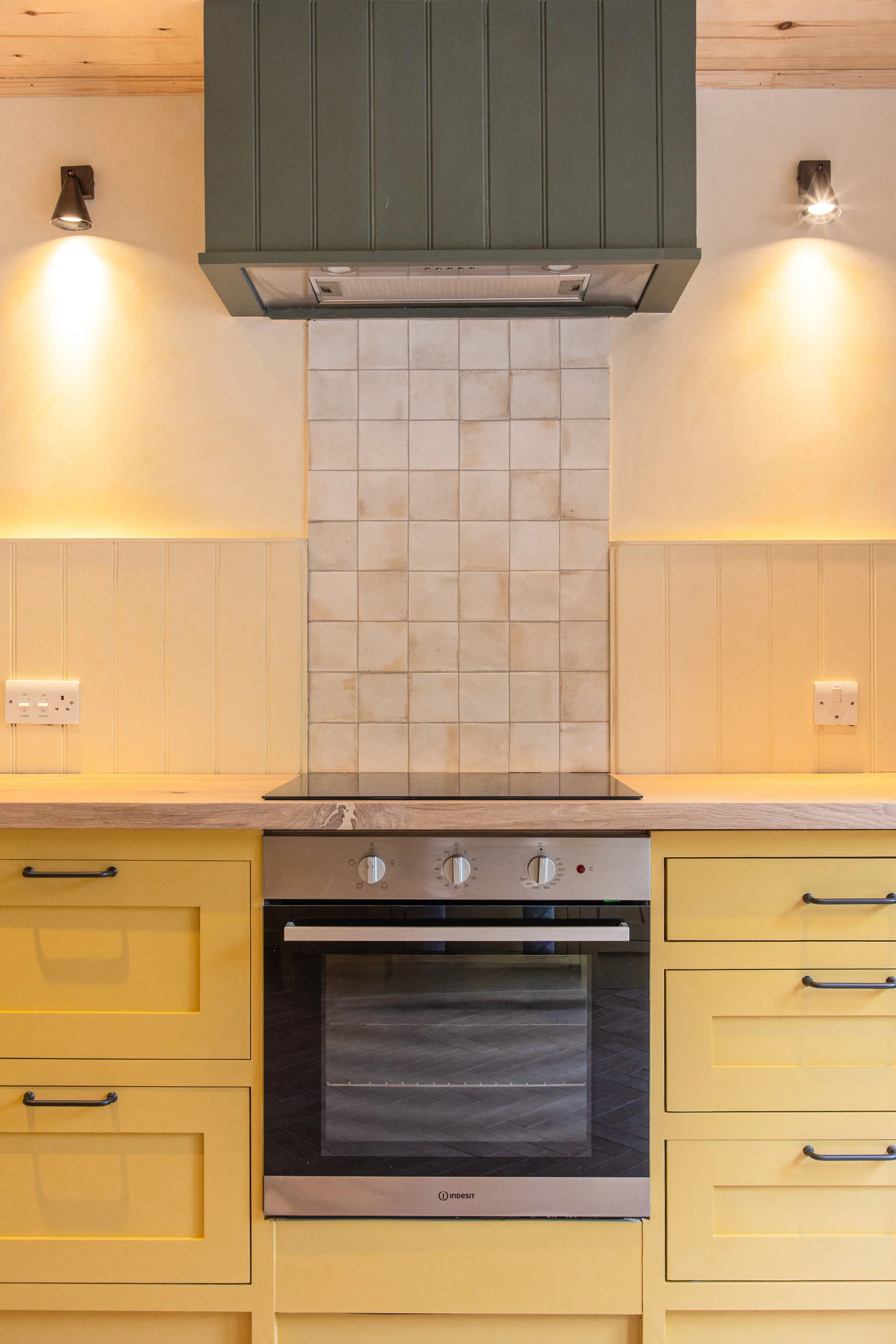 Kitchen stove and oven with hand painted yellow cabinets, tiled backsplash, and wall-mounted lights.
