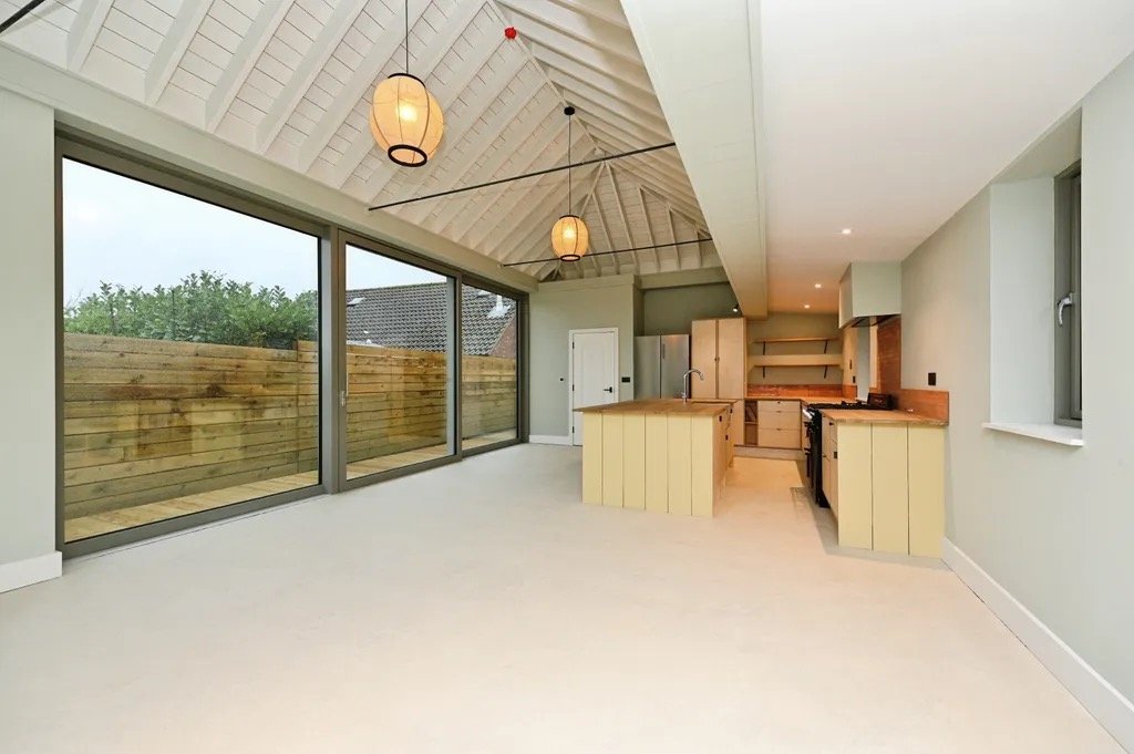Beautiful modern kitchen with bespoke birch ply cabinets, iroko wooden countertops, large glass triple glazed Norrsken sliding doors, and a vaulted ceiling with hanging light fixtures.