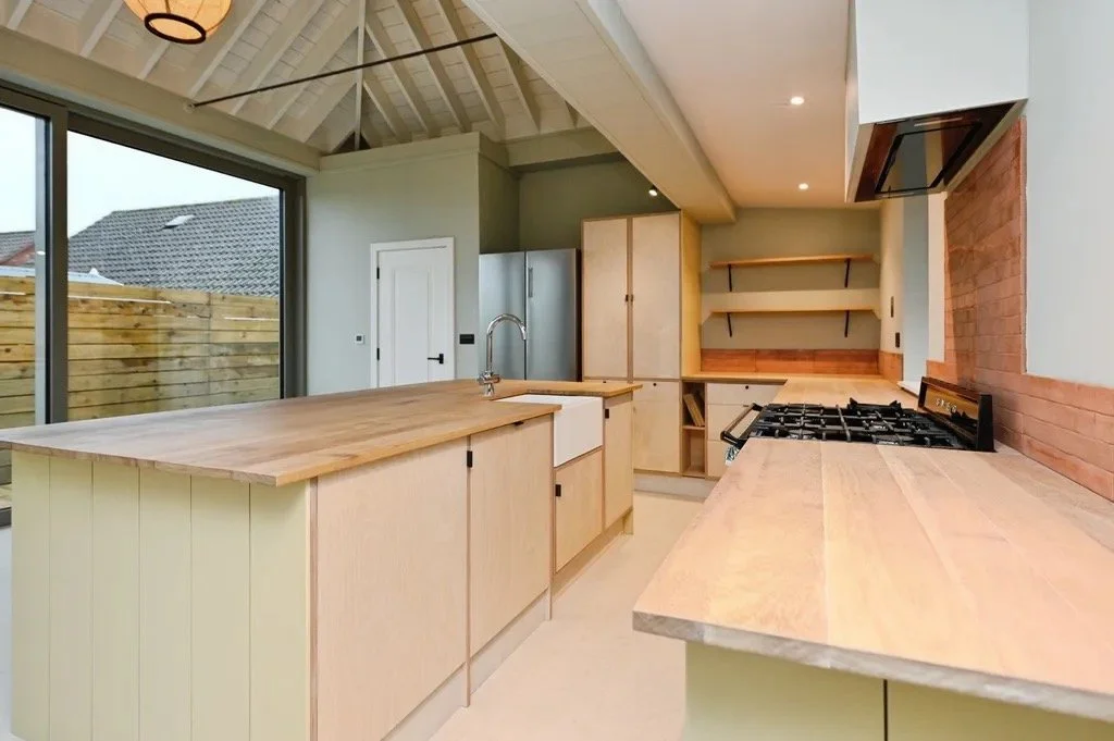 Modern kitchen with wooden countertops, a stove, and open shelves, overlooking a backyard through sliding glass doors.