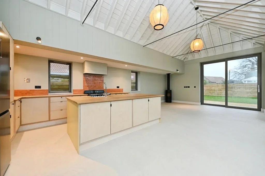 Empty modern kitchen and dining area with high vaulted ceiling, hanging pendant lights, large sliding glass doors, and a view of the backyard.
