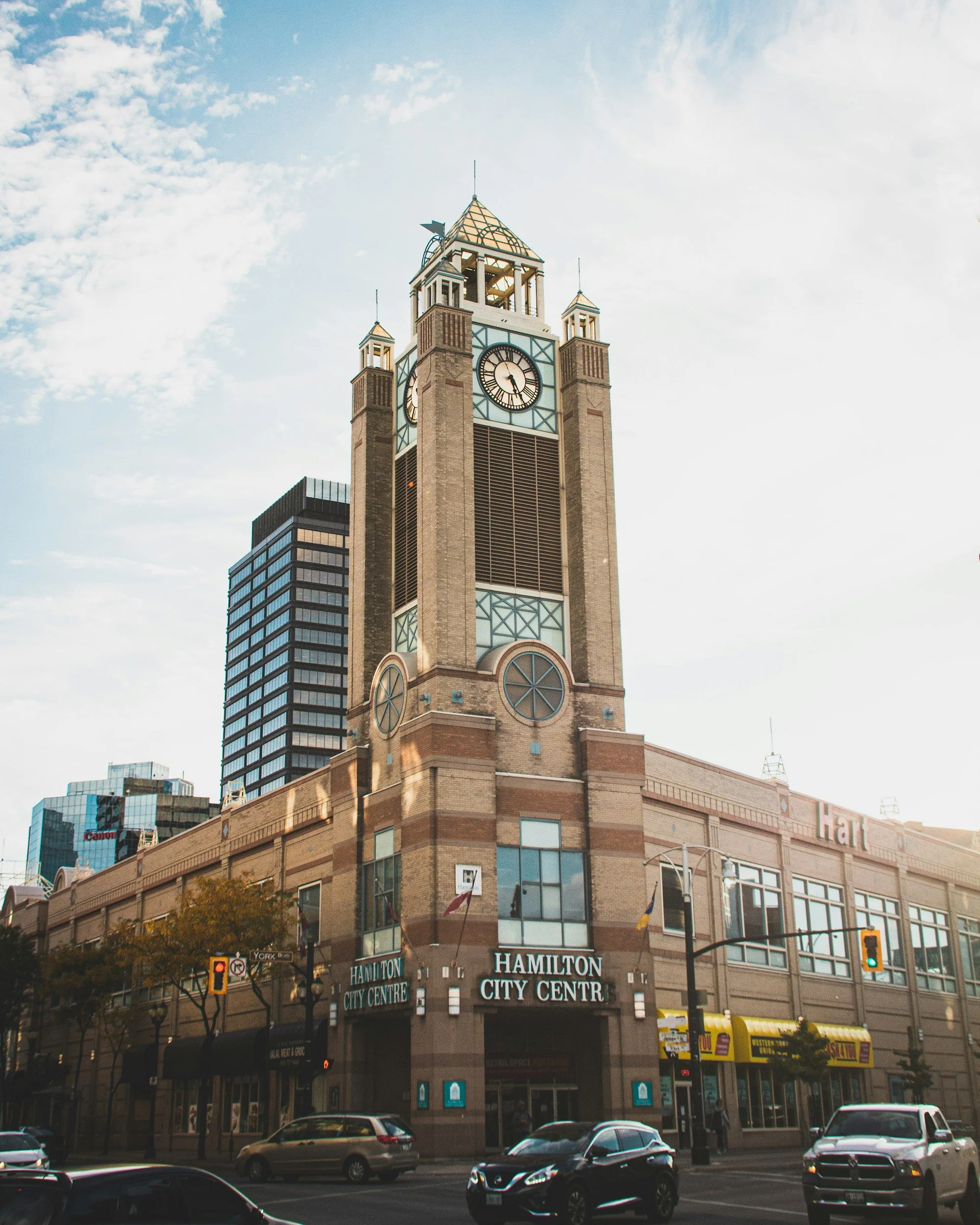 The Hamilton City Centre building with a tall clock tower, surrounded by cars and pedestrians in an urban setting, under a partly cloudy sky.