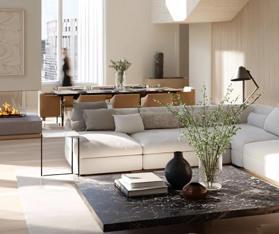 Modern living room with white sectional sofa, black marble coffee table with vases and books, floor lamp, large windows with city view, and a dining area in the background.