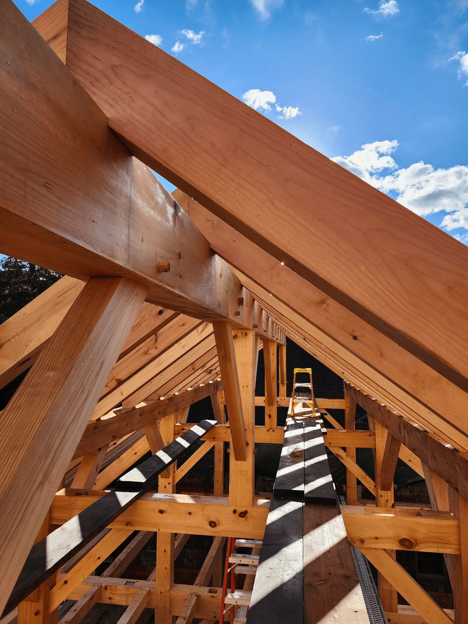 Wooden roof framing construction with a ladder and blue sky in the background.