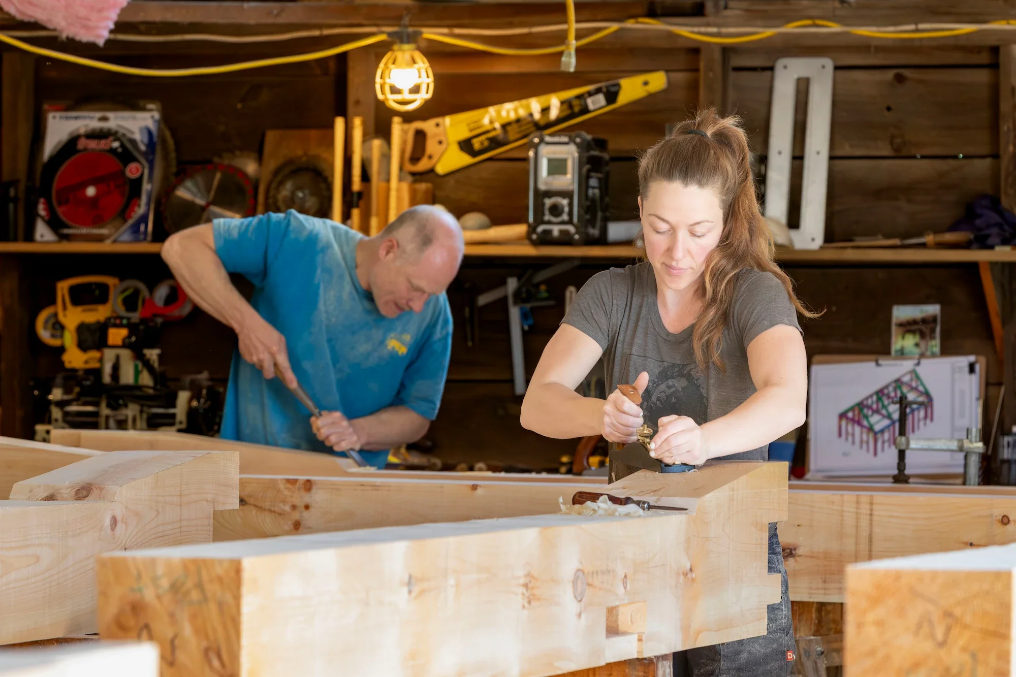 A man and a woman working on woodworking projects in a workshop filled with tools and equipment.