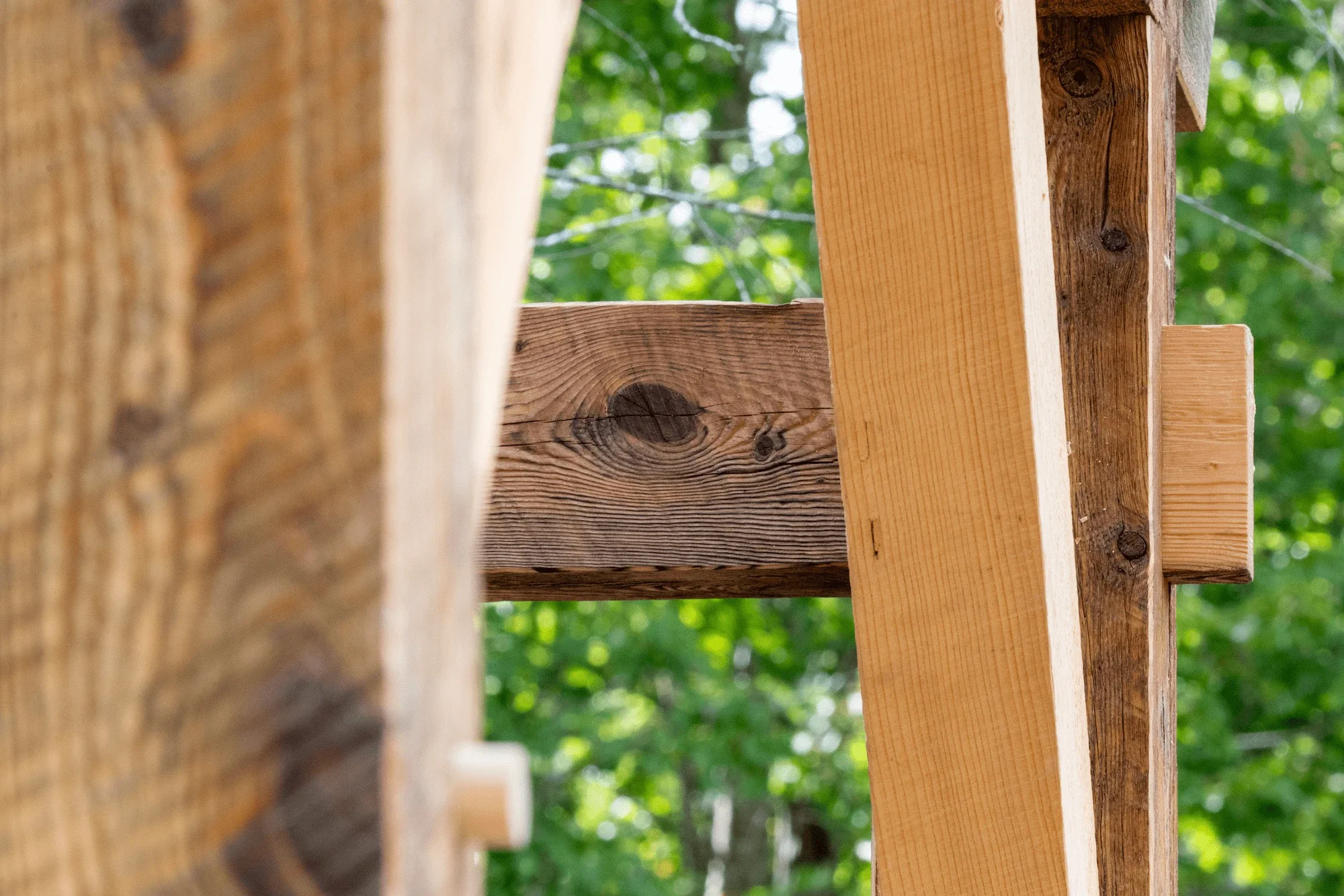 Close-up of a construction site showing wooden beams with green foliage in the background.