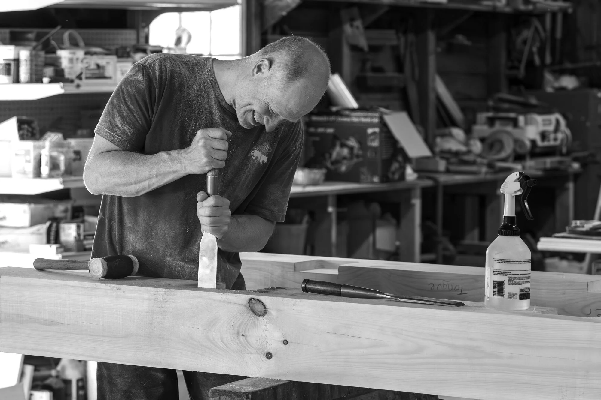 A man working on a woodworking project in a workshop, using a hammer on a piece of wood.