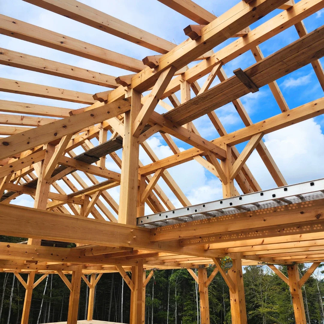 Wooden house frame under construction against a partly cloudy sky with trees in the background.
