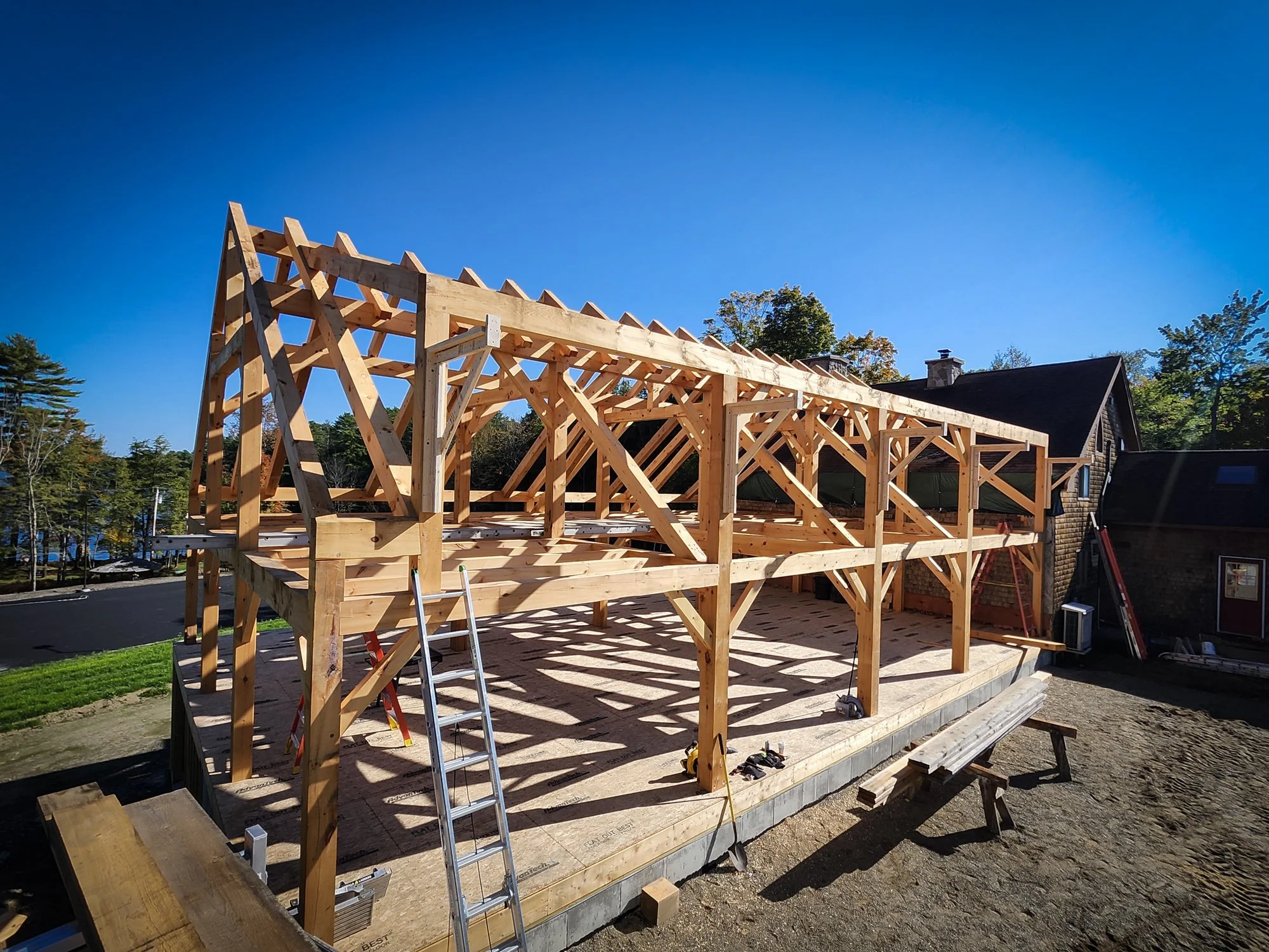 Wooden house frame under construction with scaffolding and tools on a clear sunny day.