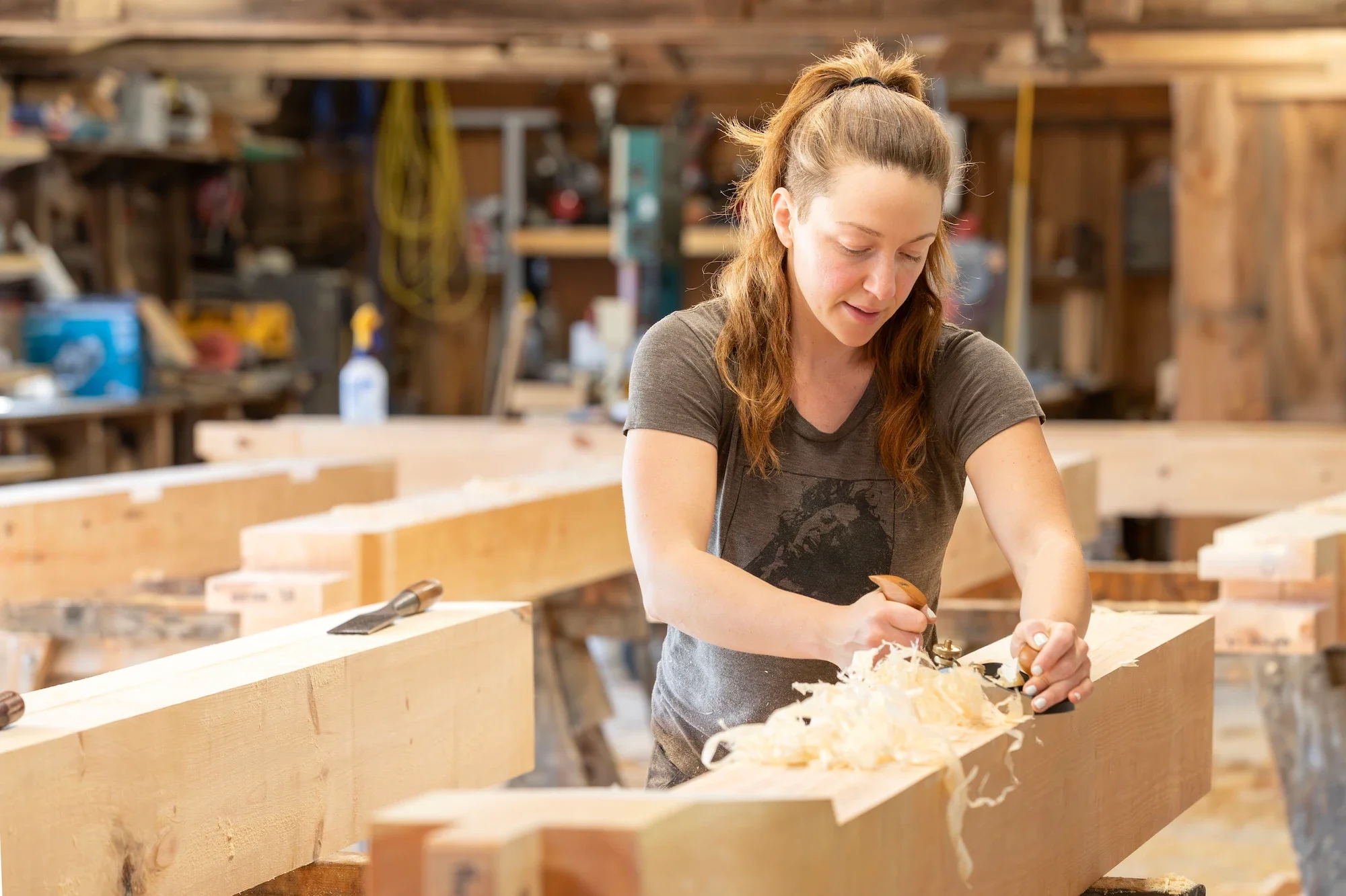 A woman woodworking in a workshop with wood shavings on a large piece of lumber.