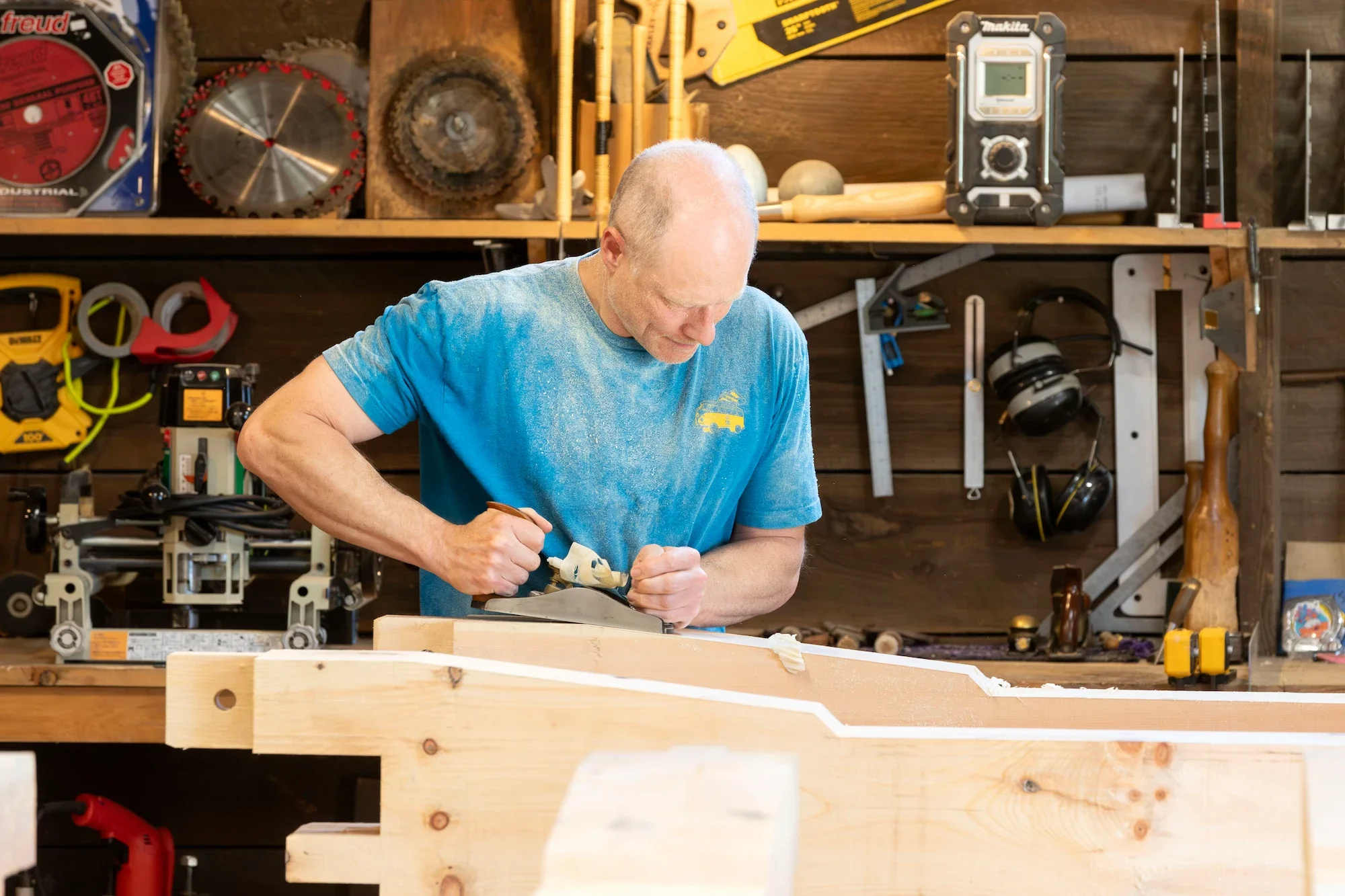 A man working on a woodworking project in a workshop, using a hand plane on a piece of wood.