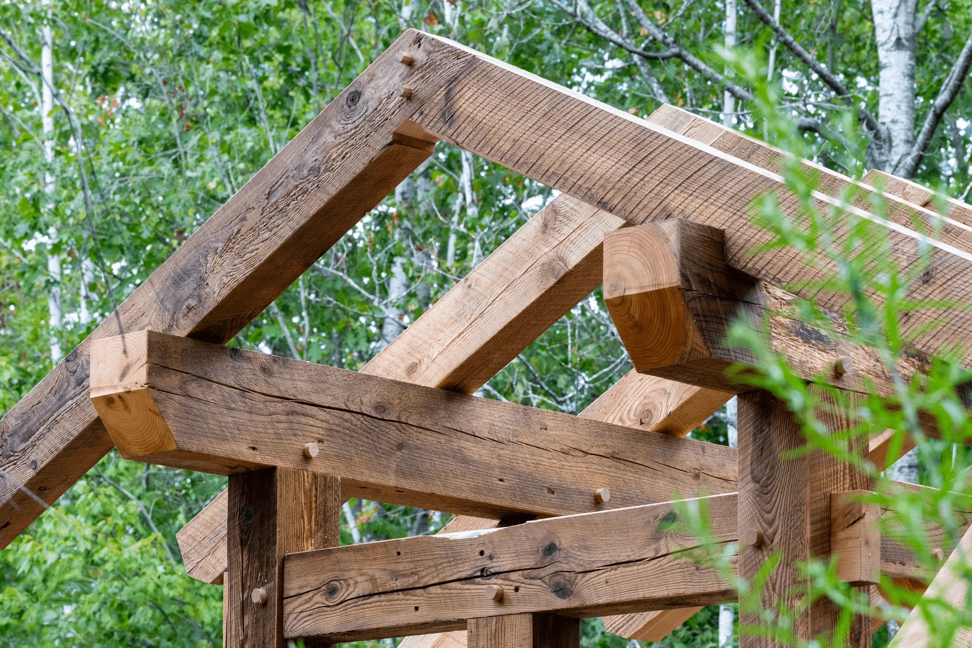 Close-up of a wooden structure framework under construction in a green outdoor setting.
