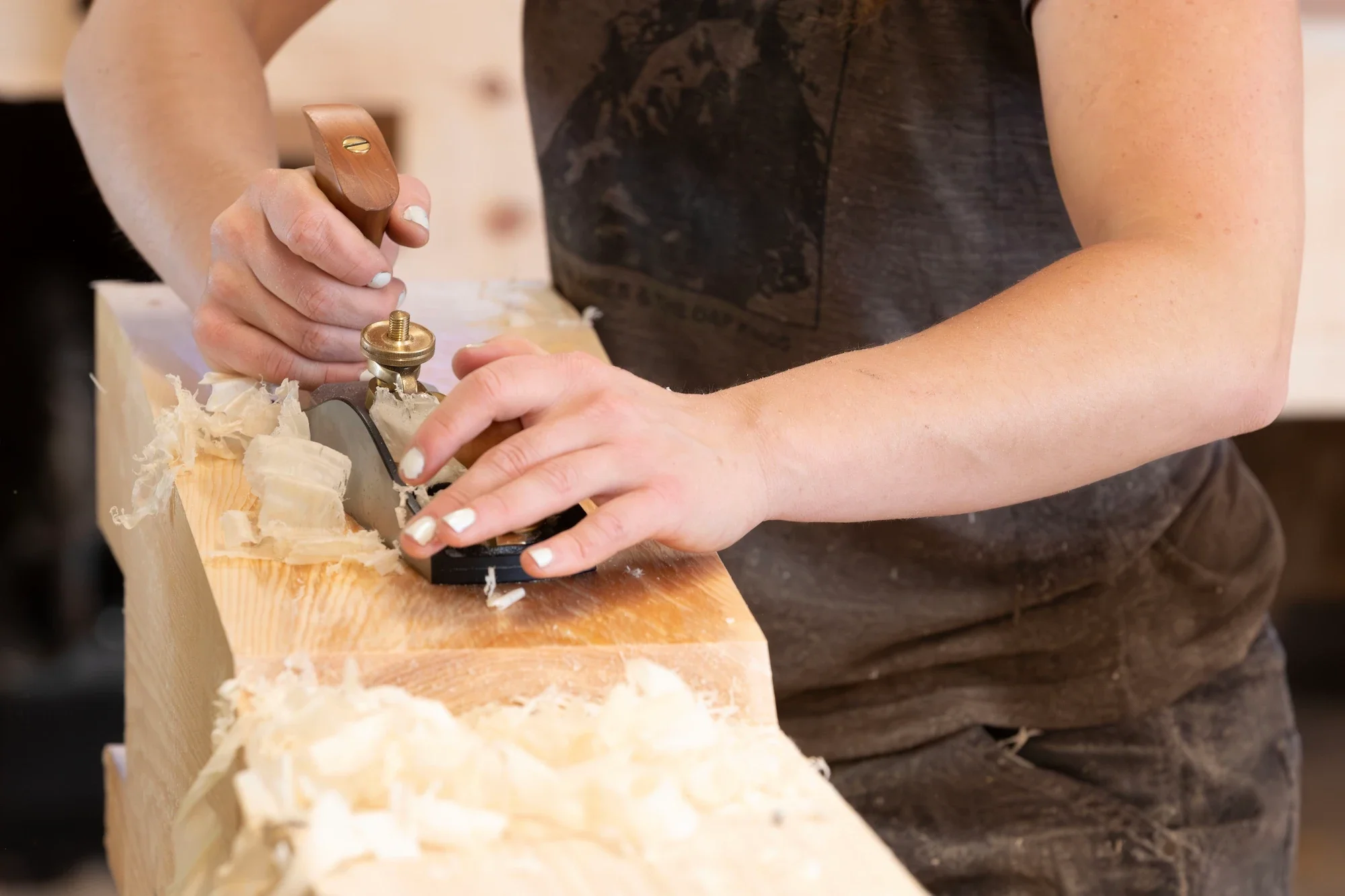 Person using a hand plane on a piece of wood in a woodworking shop.