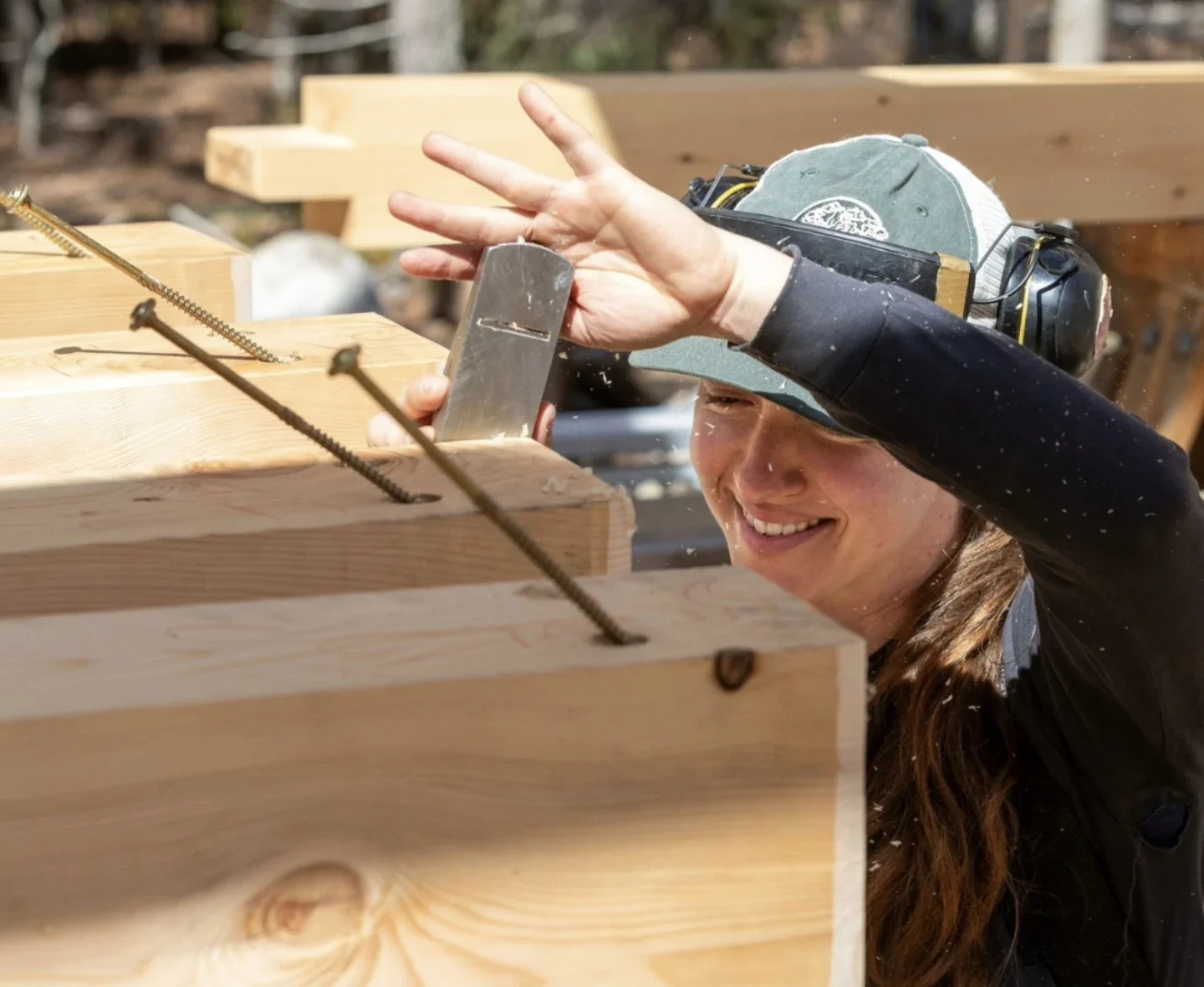 Woman smiling while working with wood and rebar on a woodworking project outdoors.