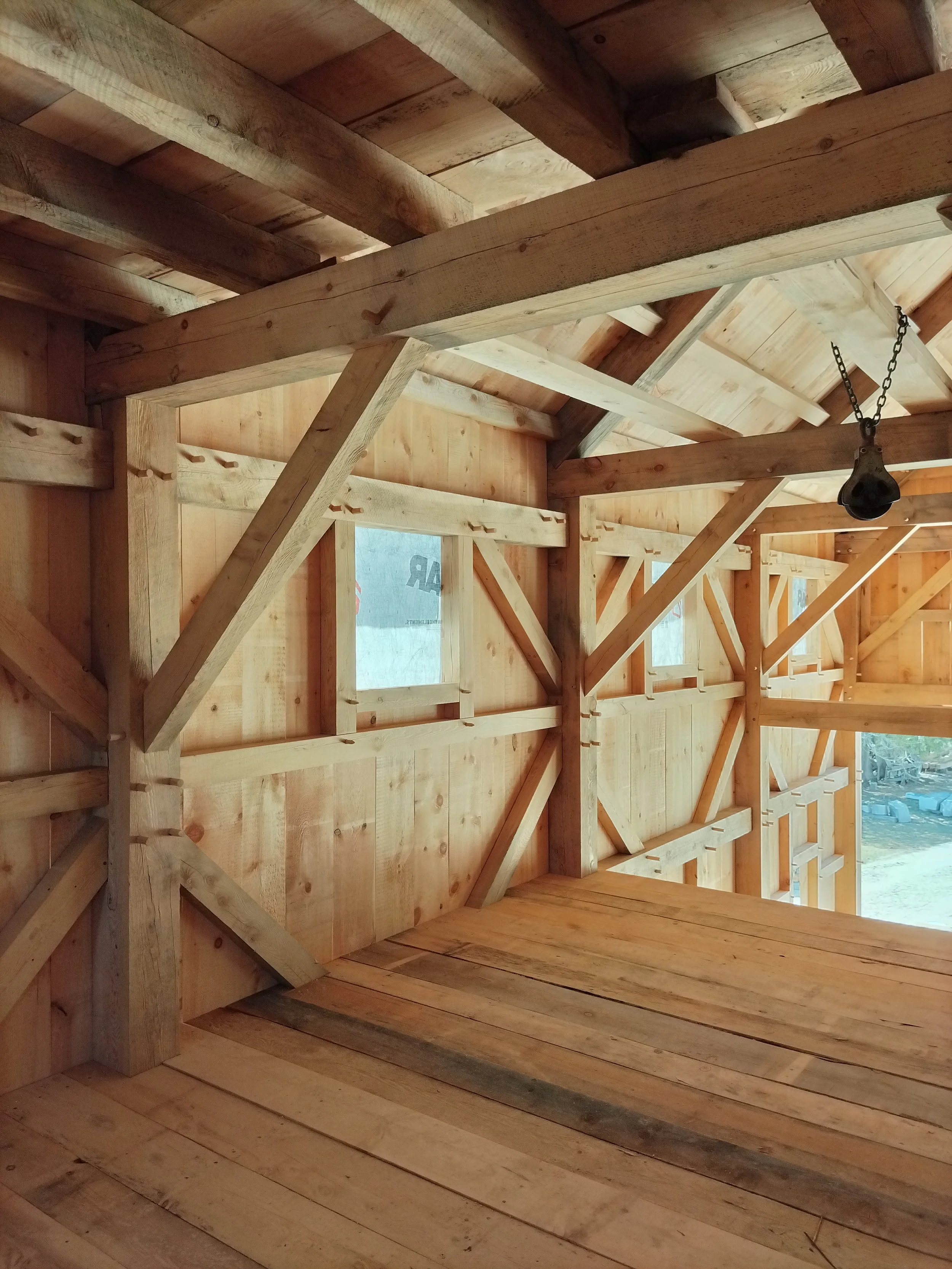 Interior view of a wooden framework structure under construction, showing unfinished walls, ceiling, and opening for a window.