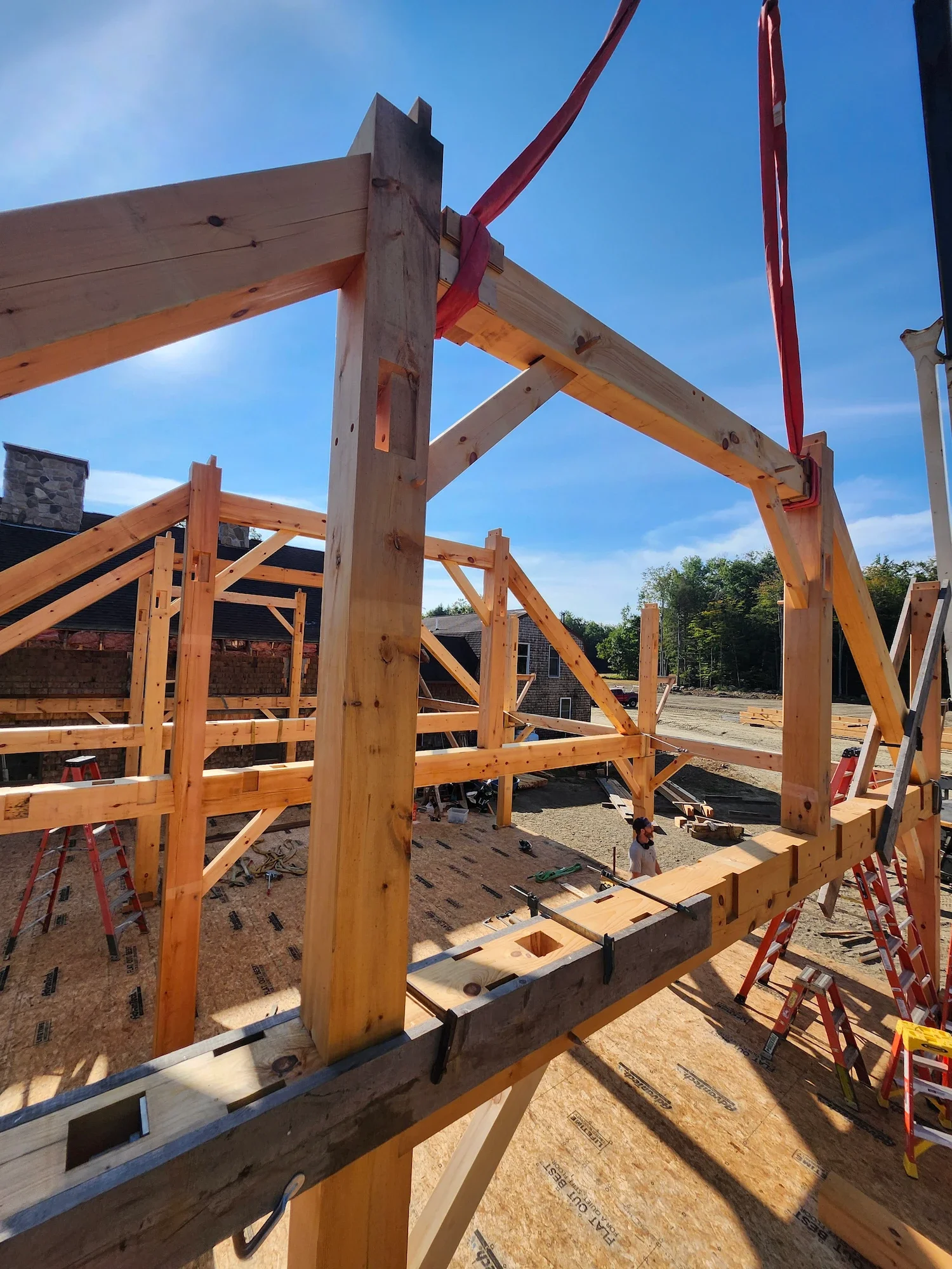 Wooden framing construction site with ladders, construction tools, and workers building a structure on a clear sunny day.