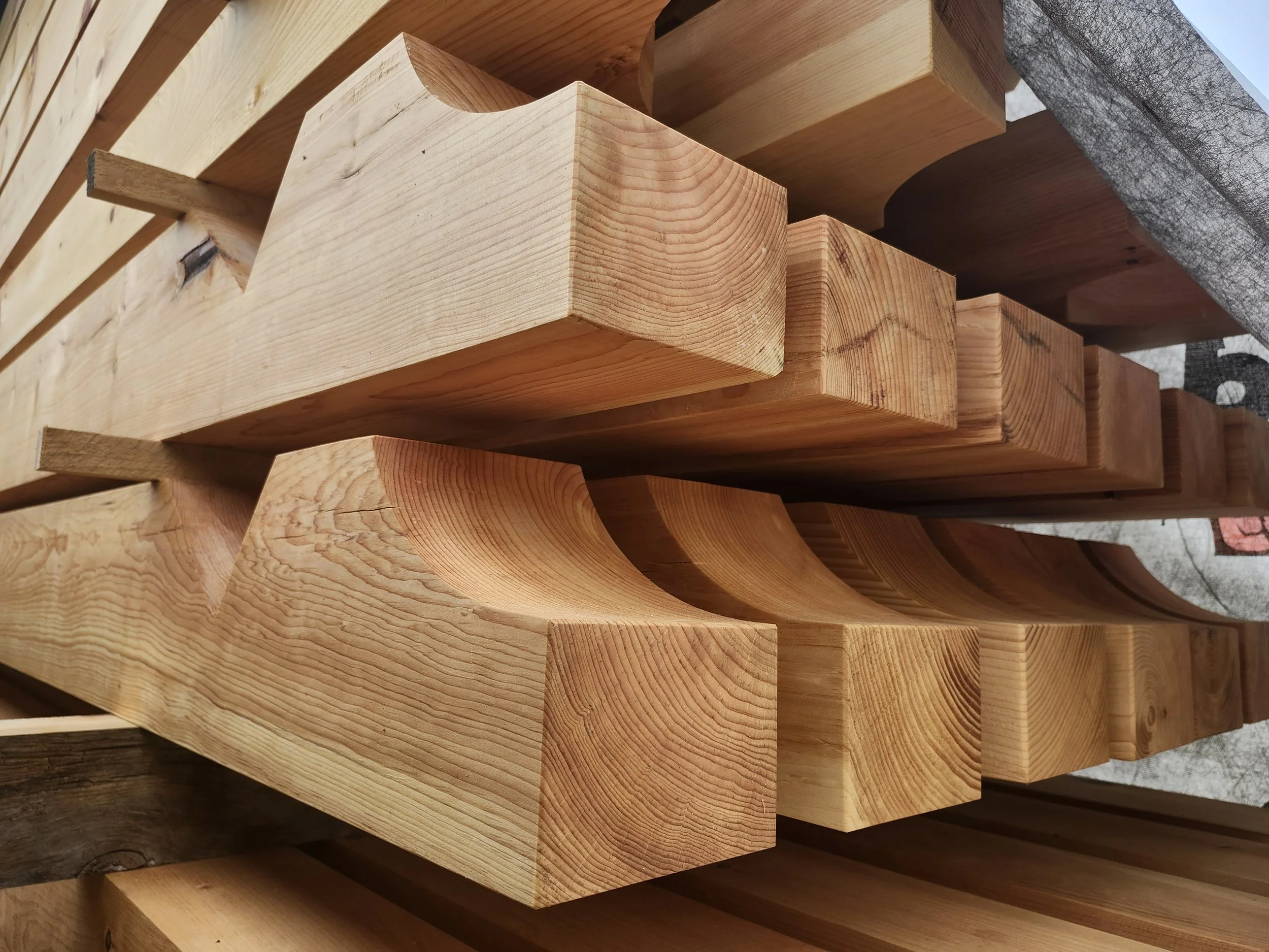 Stacked wooden beams with intricate grain patterns and curved cuts, ready for construction.