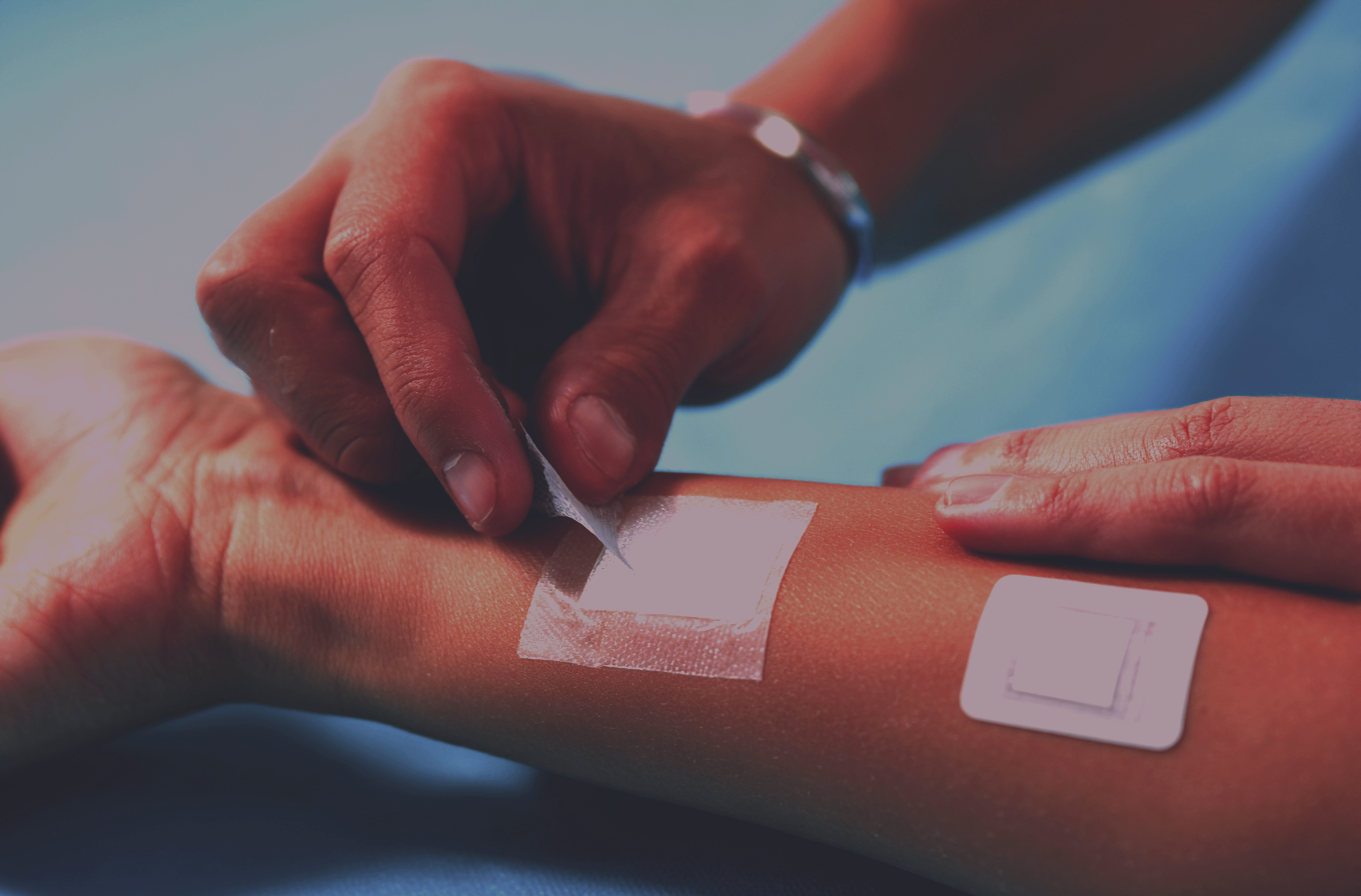 Close-up of a person's arm with a medical bandage and a dressing change being applied by healthcare professional.