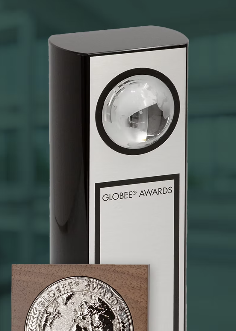 A silver Globee Award trophy with a globe design displayed on a wooden base, beside a tall black and gray award trophy with a spherical glass element and the text "GLOBEE® AWARDS" on the front.