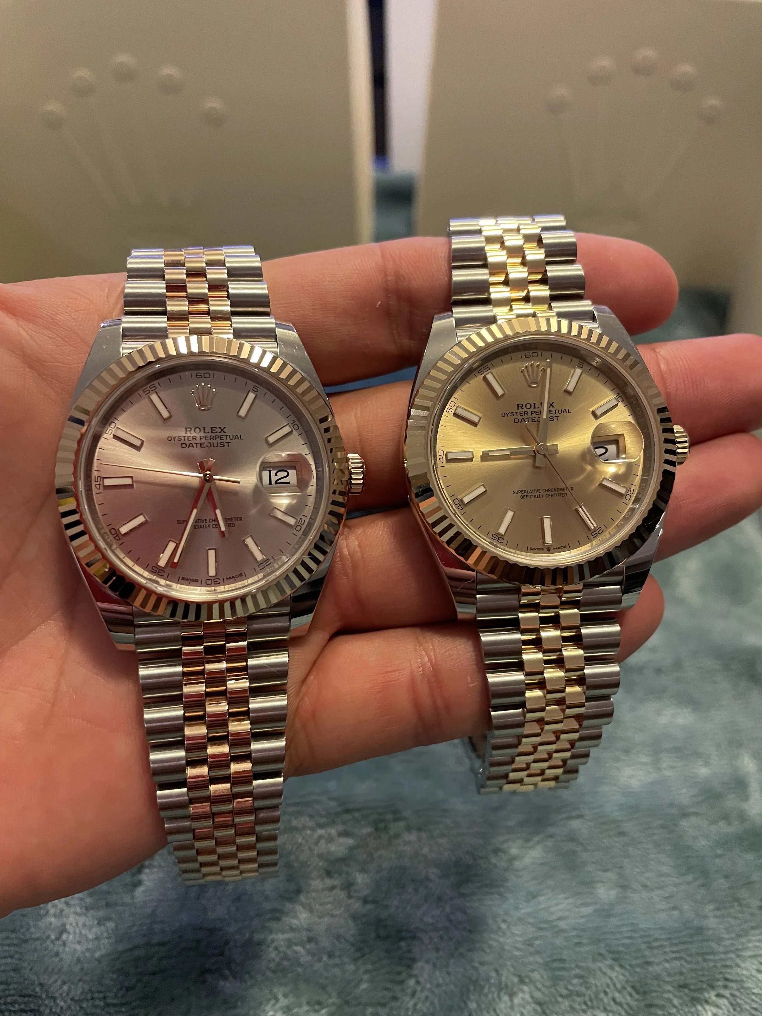 Two Rolex watches with silver and gold bands, one with a silver face and the other with a gold face, held in a person's hand.