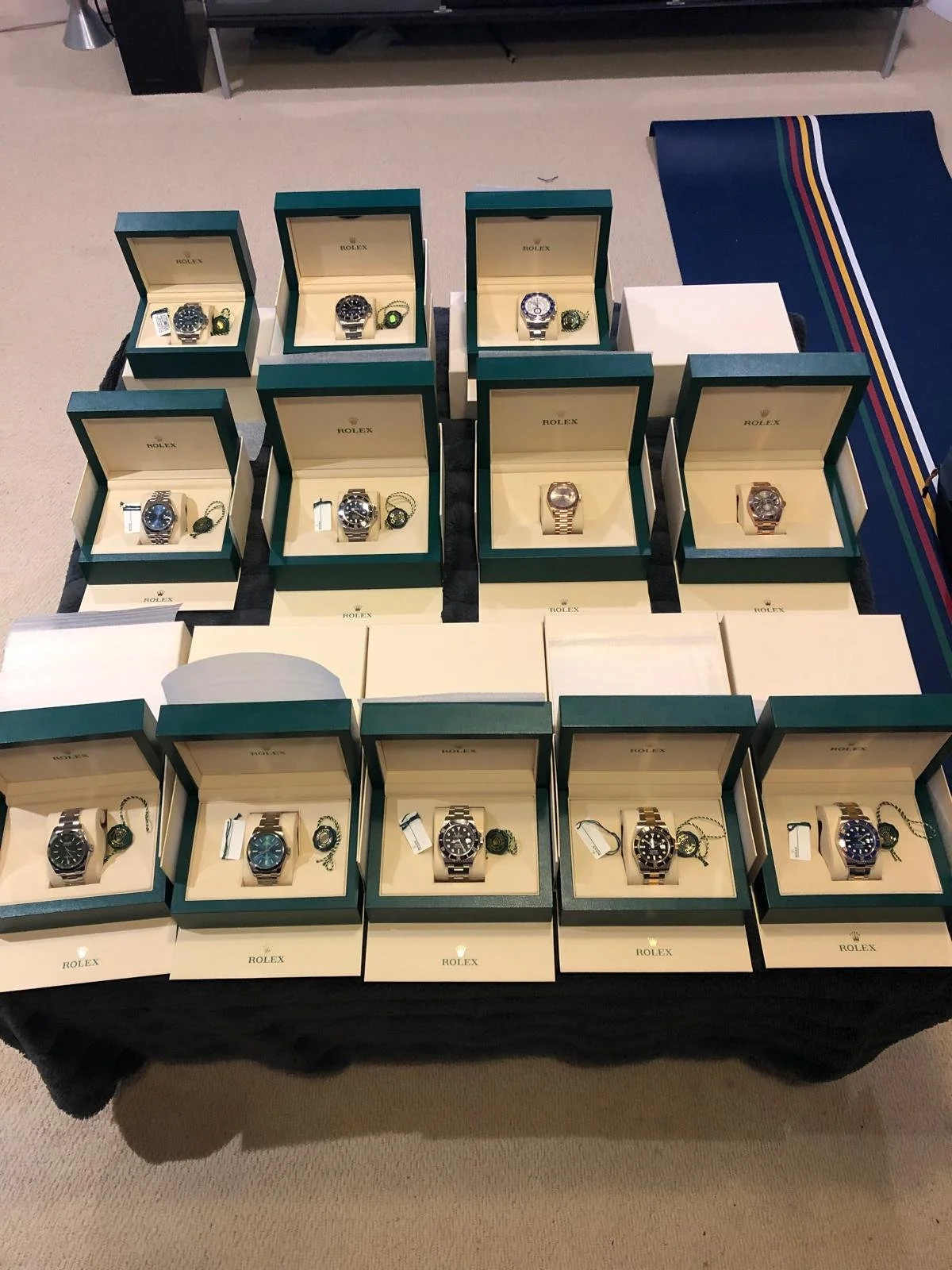 A table displaying multiple Rolex watches in green and cream boxes, arranged in rows.