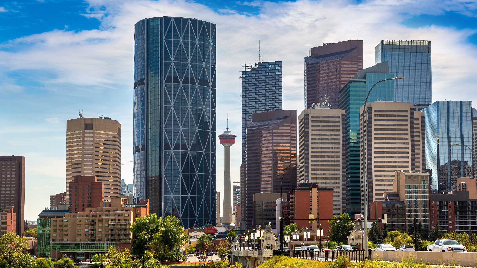 Skyline of downtown Calgary, Alberta with tall modern office buildings and the Calgary Tower in the center, under a partly cloudy sky.