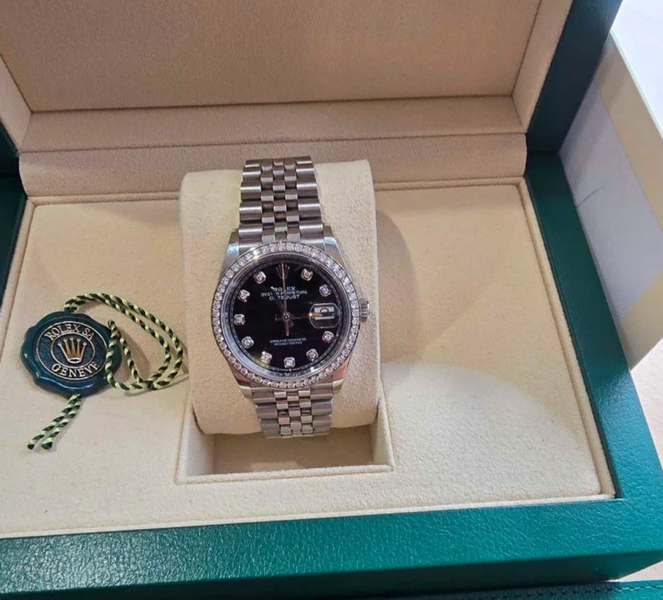 Luxury Rolex watch with a black face, diamond hour markers, and a stainless steel band in a green box.