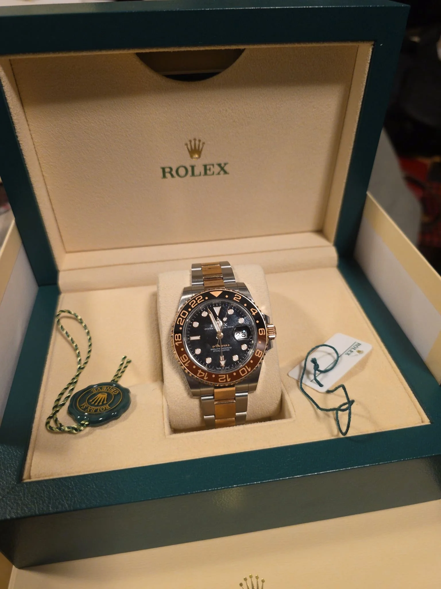 A Rolex watch inside its green and beige box, with tags attached.