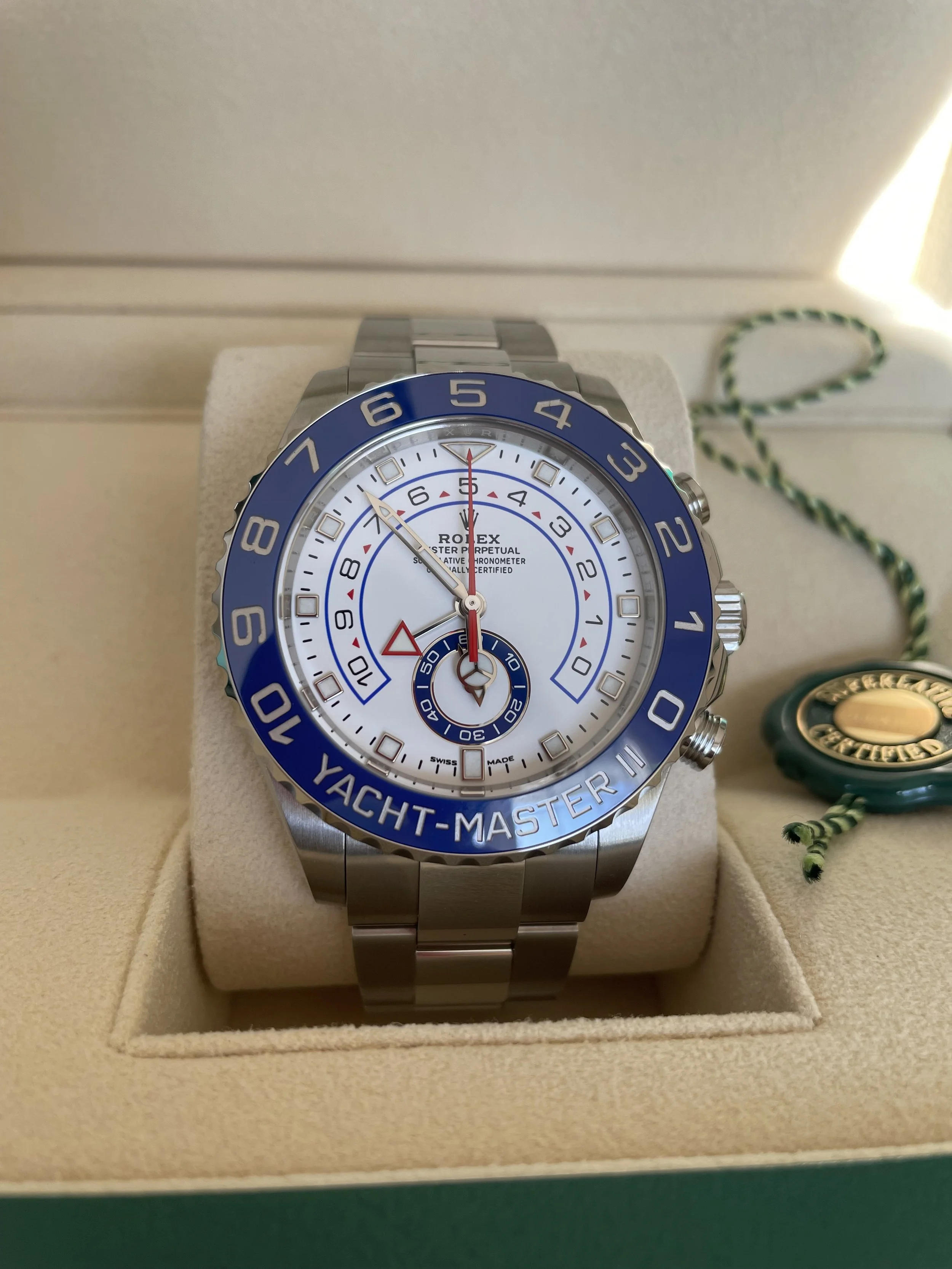 A Rolex Yacht-Master II wristwatch with a blue bezel, white dial, and stainless steel band, displayed in a beige watch case.