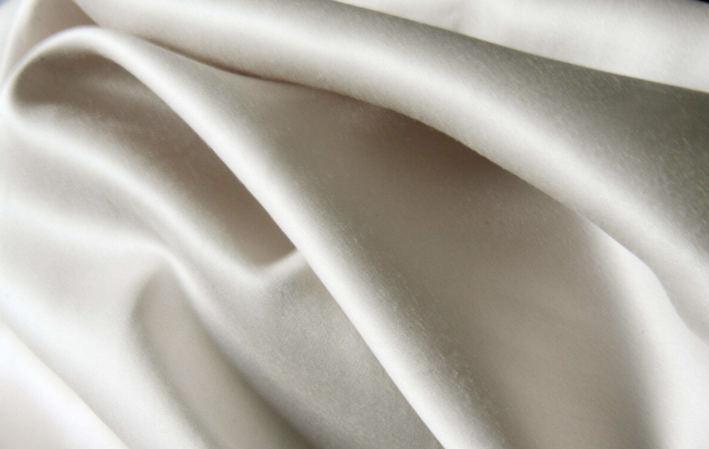 Close-up of smooth, shiny, off-white satin fabric with gentle folds.