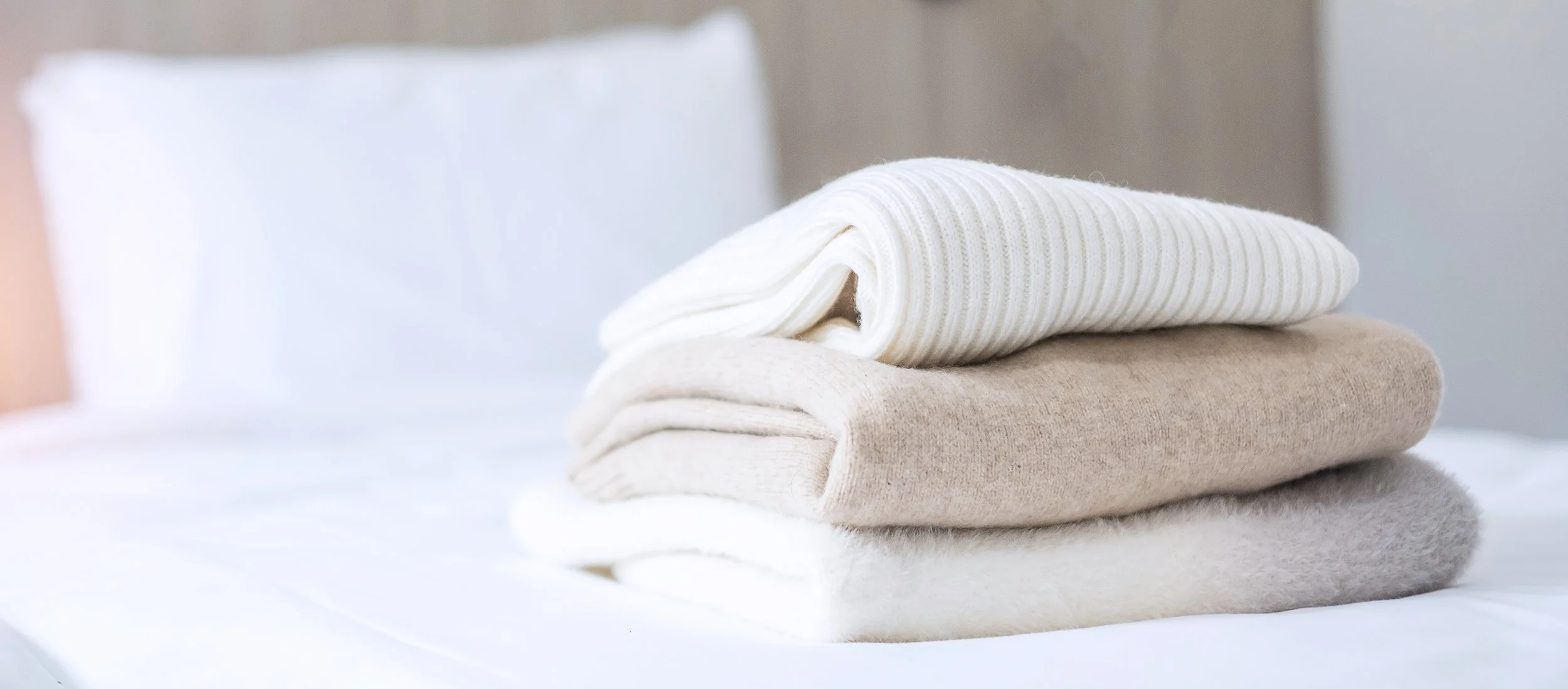 Stacked beige and white folded sweaters on a white surface