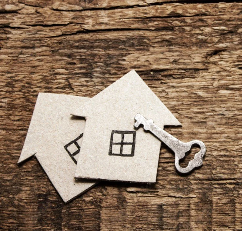 Small house-shaped paper cutouts with window drawings, a metal key, on a wooden surface.