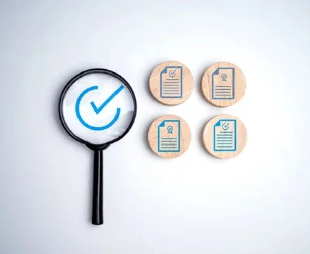 Magnifying glass with a blue checkmark and four wooden tokens with document icons on a white background.