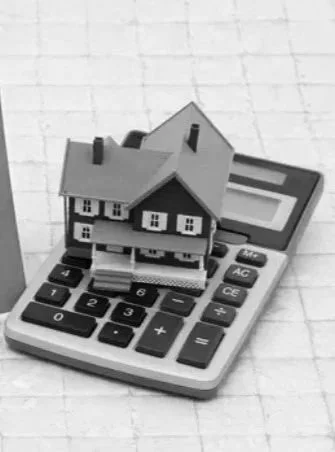 A miniature house model placed on a calculator with a paper grid background.