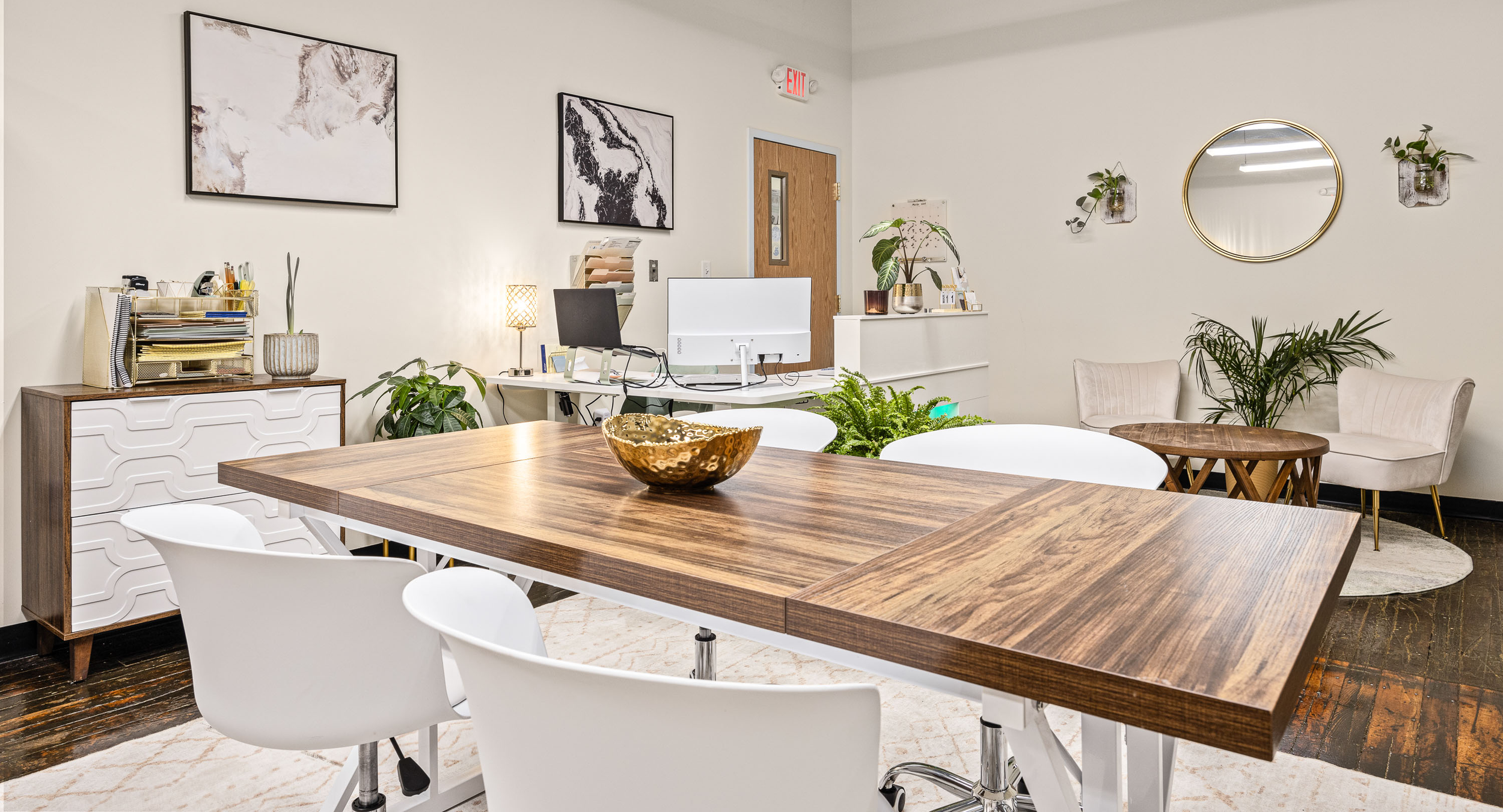 Modern office conference room with wooden table, white chairs, plants, and wall art.