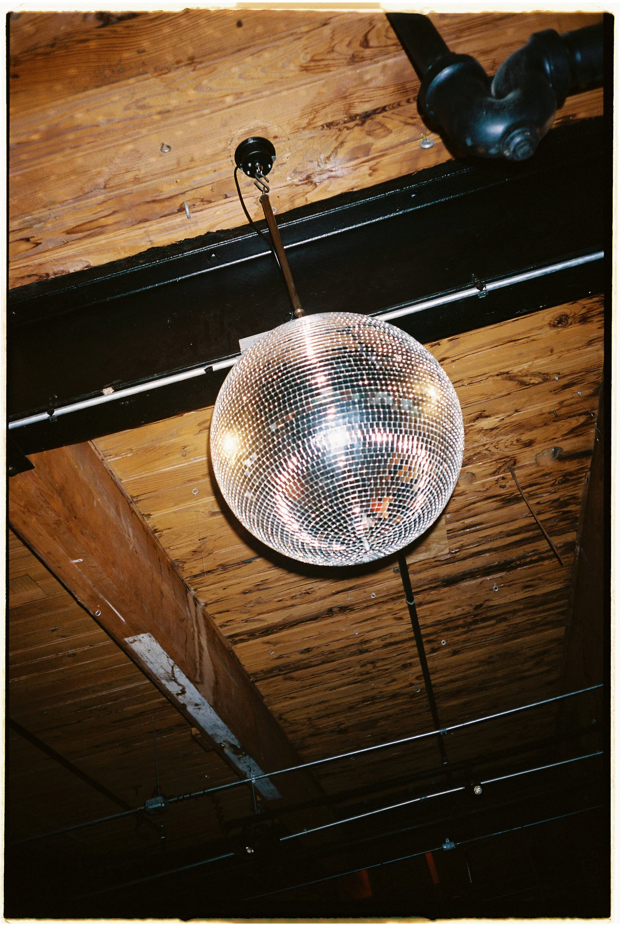 Disco ball hanging from a ceiling with wooden beams and exposed pipes.