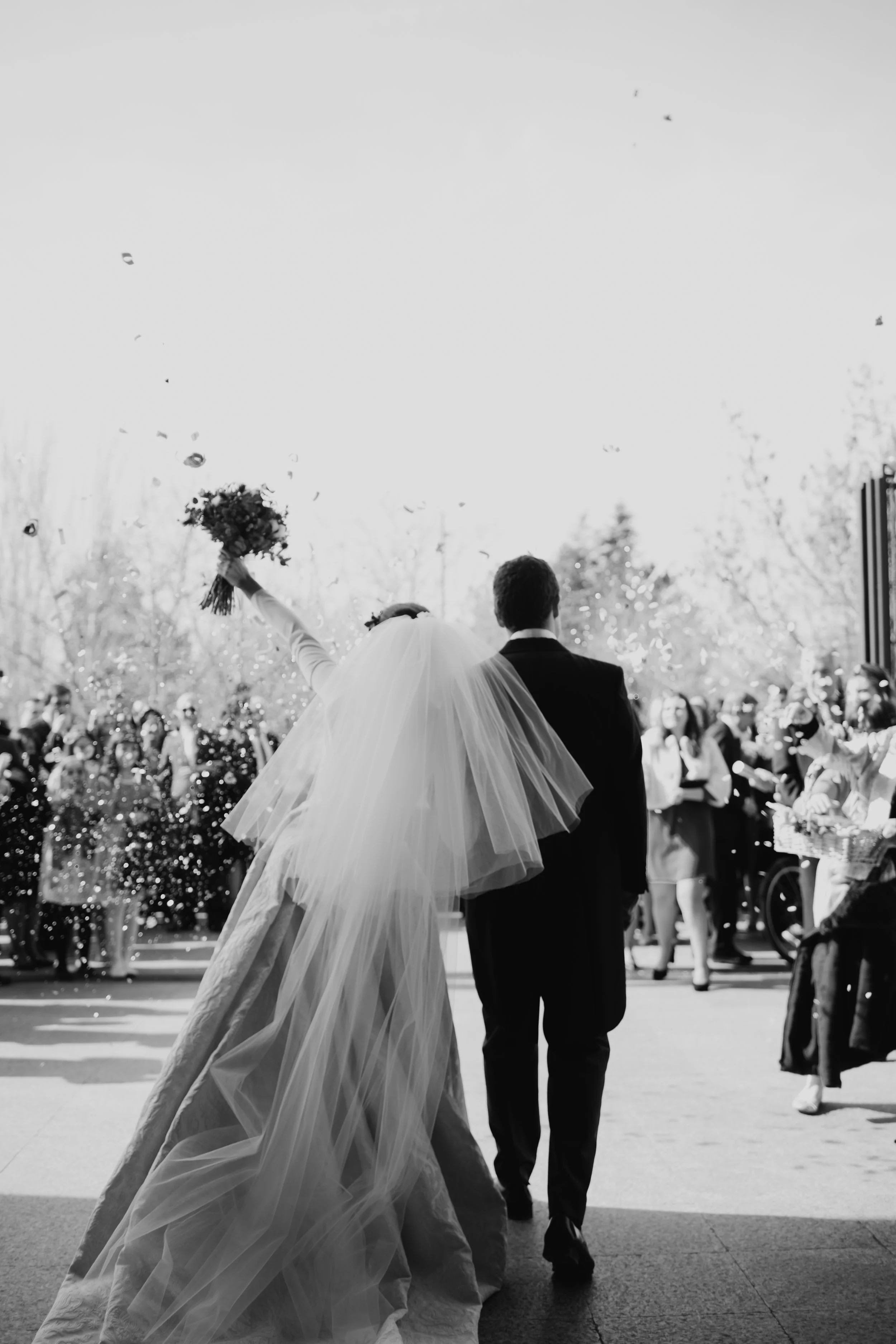 Recién casados saliendo de la iglesia y caminando entre invitados mientras la novia saluda con el ramo tras la ceremonia.