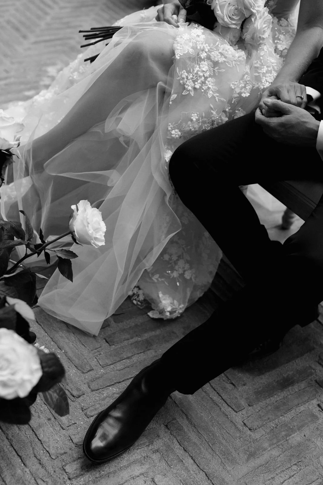 Novios sentados entre flores durante su ceremonia civil; ella lleva vestido de encaje y velo y él traje negro.