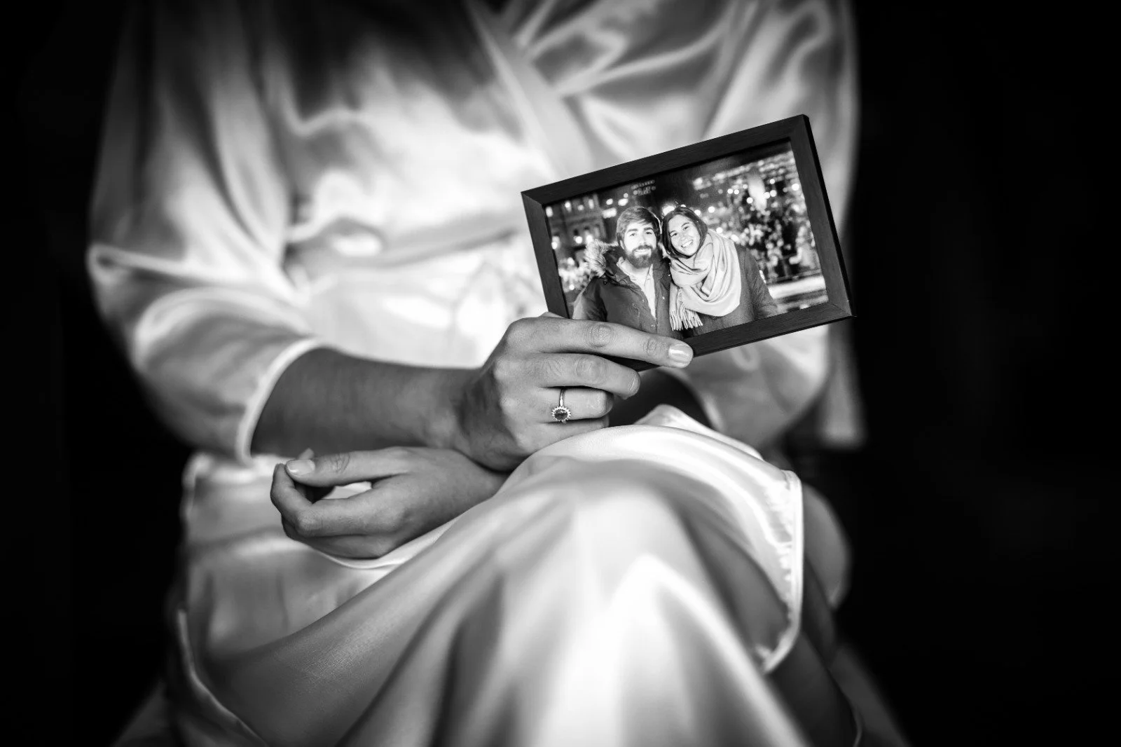 Novia en camisón sosteniendo una fotografía antigua con ella y el novio mientras se prepara para su ceremonia religiosa.
