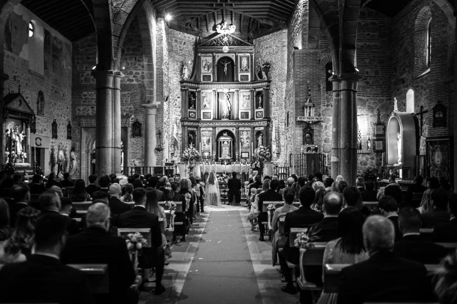 Ceremonia religiosa de boda en una iglesia, con los novios ante el altar y los invitados sentados en los bancos.
