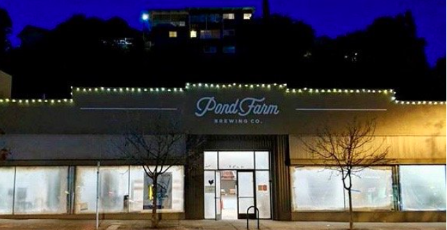Front view of Pond Farm Brewing Co. storefront at night, with string lights above the entrance and two leafless trees in front.