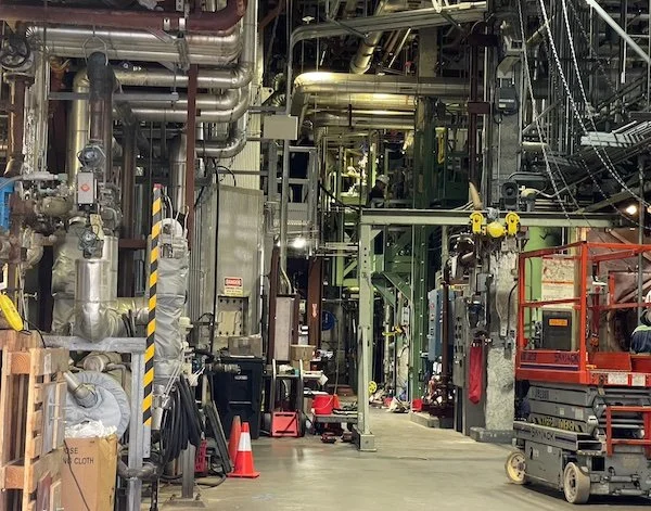 Industrial factory setting with pipes, machinery, and equipment on a factory floor.
