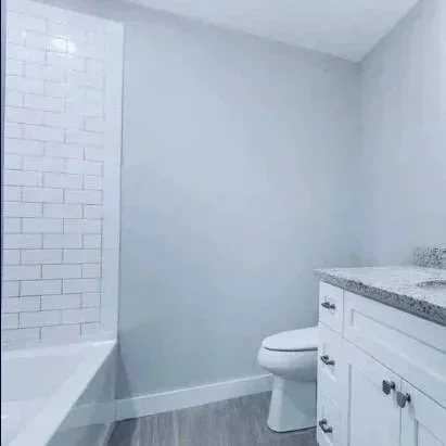 Bathroom with white subway tile shower, white vanity with granite countertop, and a toilet. Built Structure Pro in Massachusetts