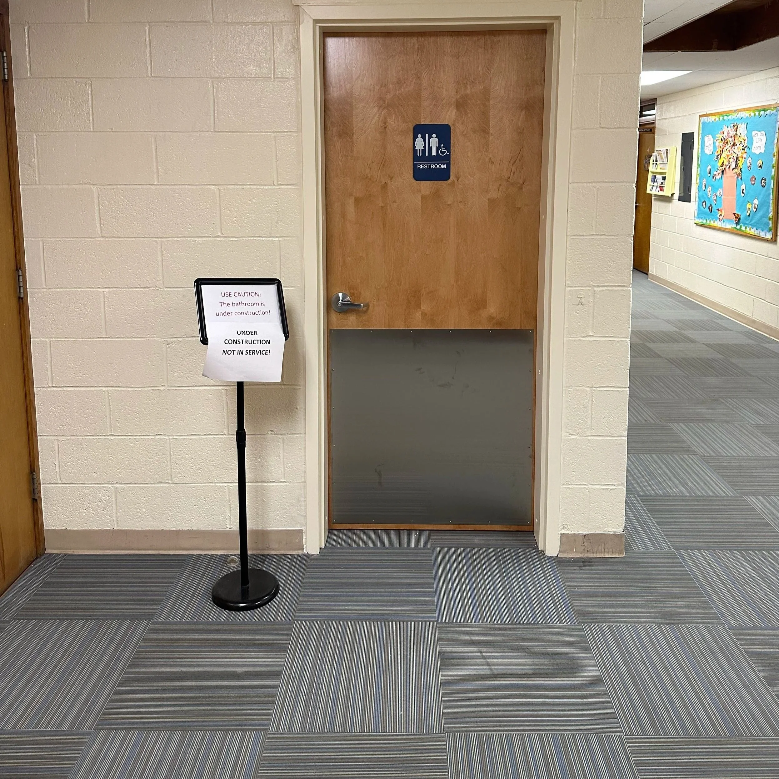 A closed wooden door with a half metal panel at the bottom; blue restroom sign with male, female, and wheelchair symbols on the door. Built Structure Pro in Massachusetts