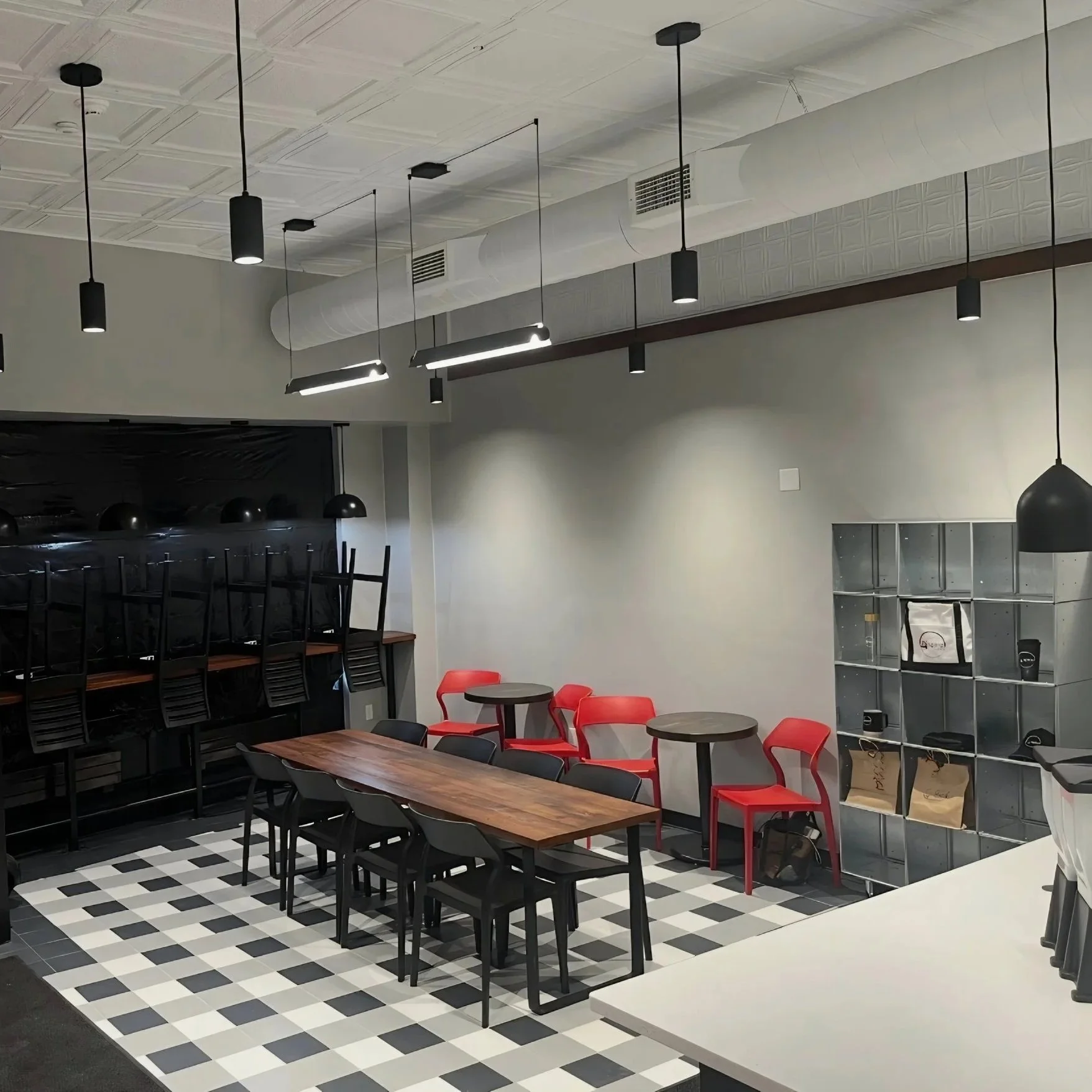 Empty modern café with black and wooden furniture, red chairs, and black pendant lighting, featuring a checkered black and white floor.