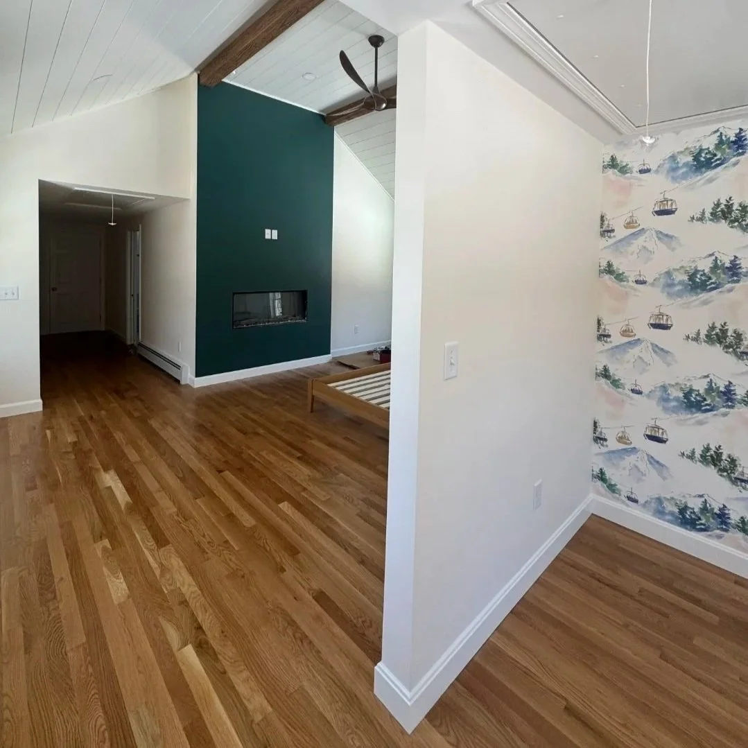 Living room with wood flooring, a teal accent wall with a modern fireplace, a ceiling fan, and a corner with a wallpaper of cable cars and mountain scenery.Built Structure Pro in Massachusetts
