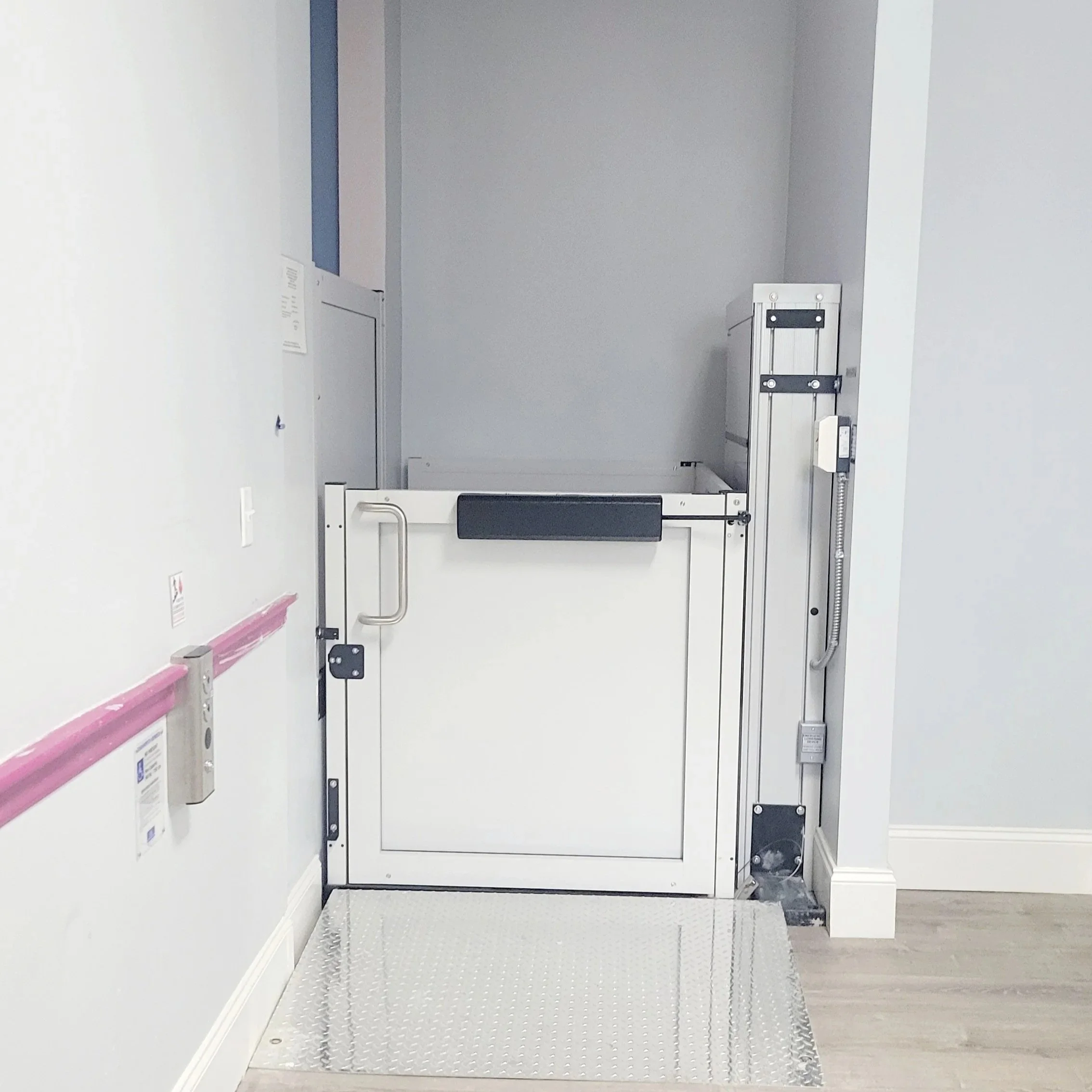 A  wheelchair lift with metal platform and sides, located in a corridor with white walls and wooden flooring at the Boys and Girls Club. Built Structure Pro in Massachusetts