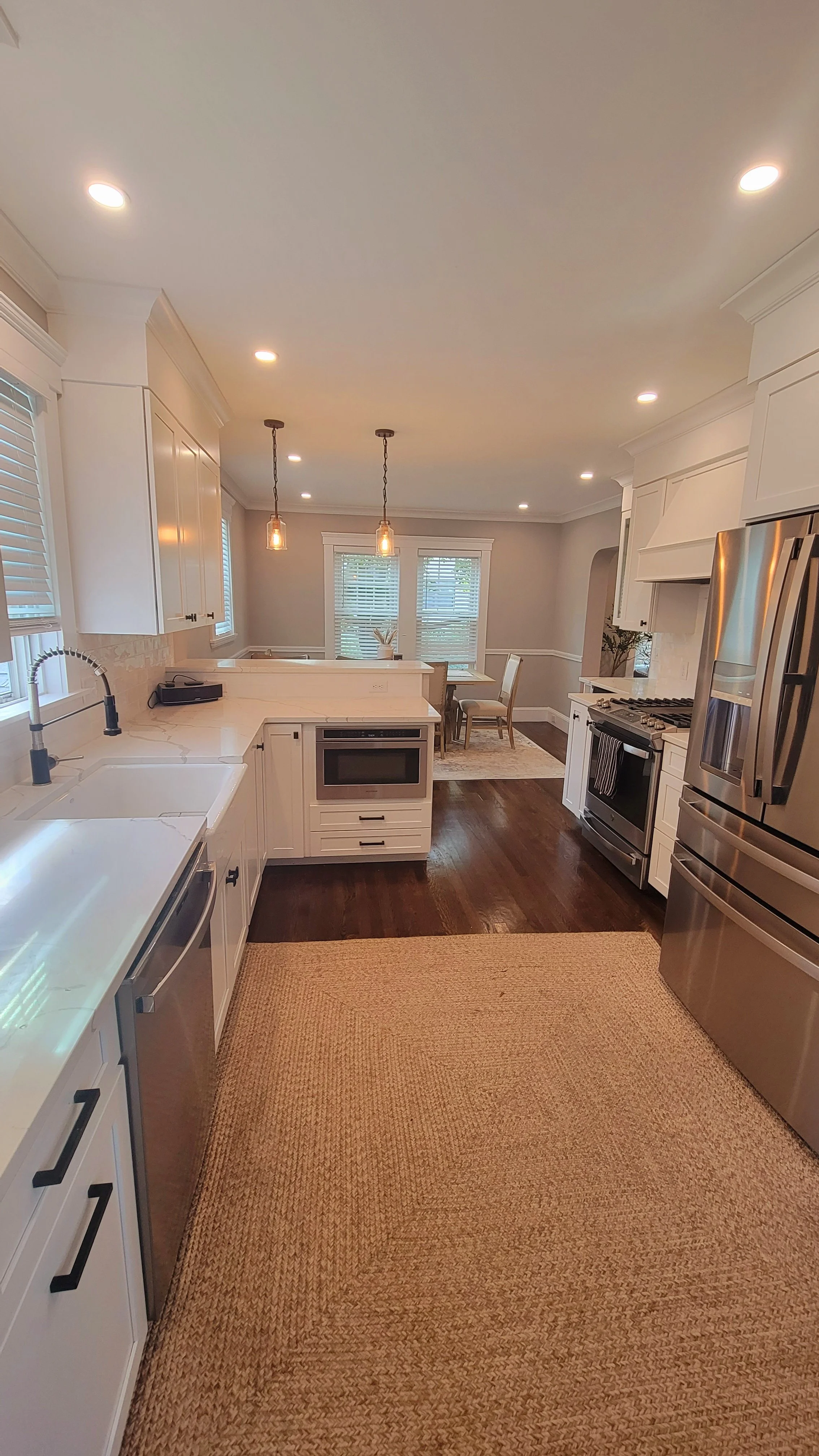 Modern kitchen with white cabinets, stainless steel appliances, dark wood flooring, and a dining area in the background with a window view. Renovated Structure Pro in Massachusetts