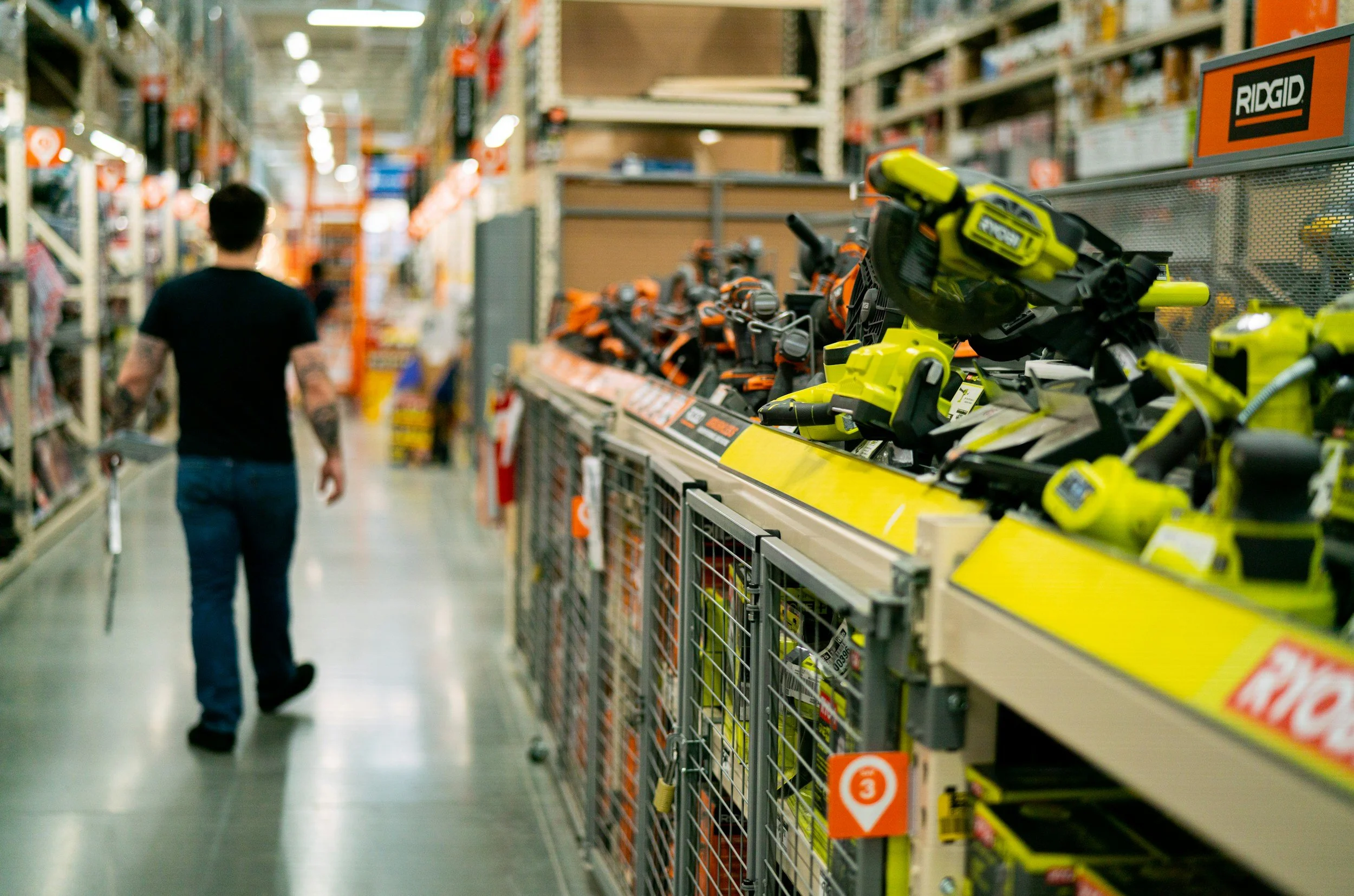 A person walking through an aisle of a hardware store with power tools displayed on the shelves.
