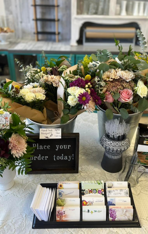 Bouquets of fresh flowers on display at a flower shop, with a sign to place orders and greeting cards nearby.