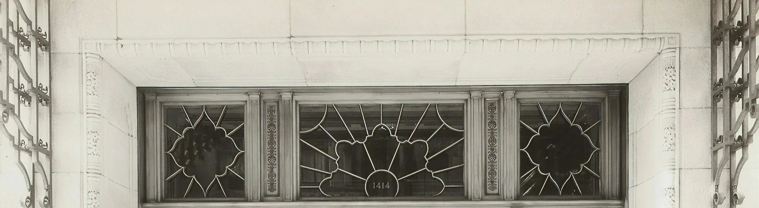 Close-up of art-deco stained glass windows with geometric patterns and the number 1414 at the center.